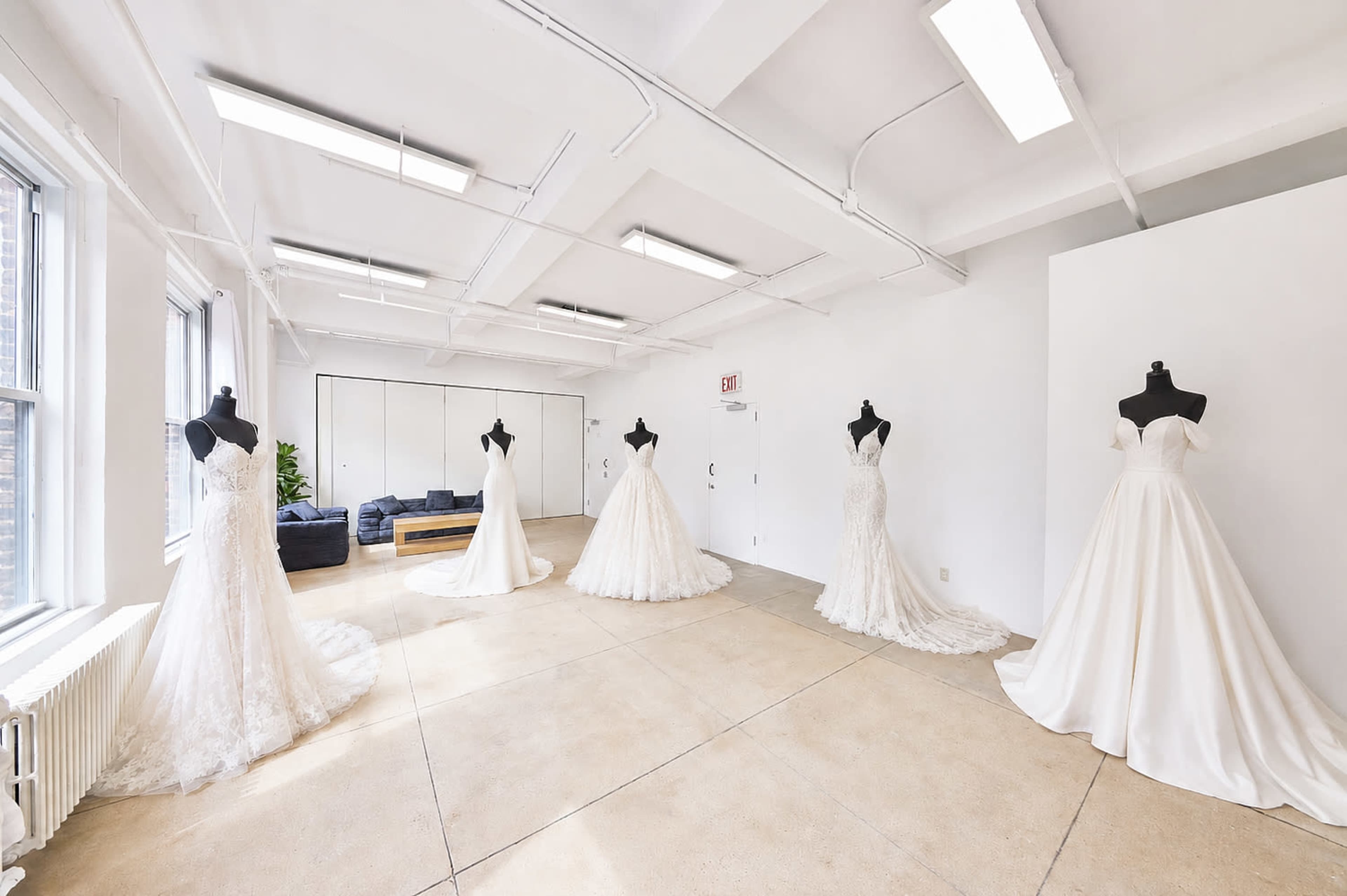 The image shows a spacious, bright room with five wedding dresses displayed on mannequins arranged in a semi-circle.