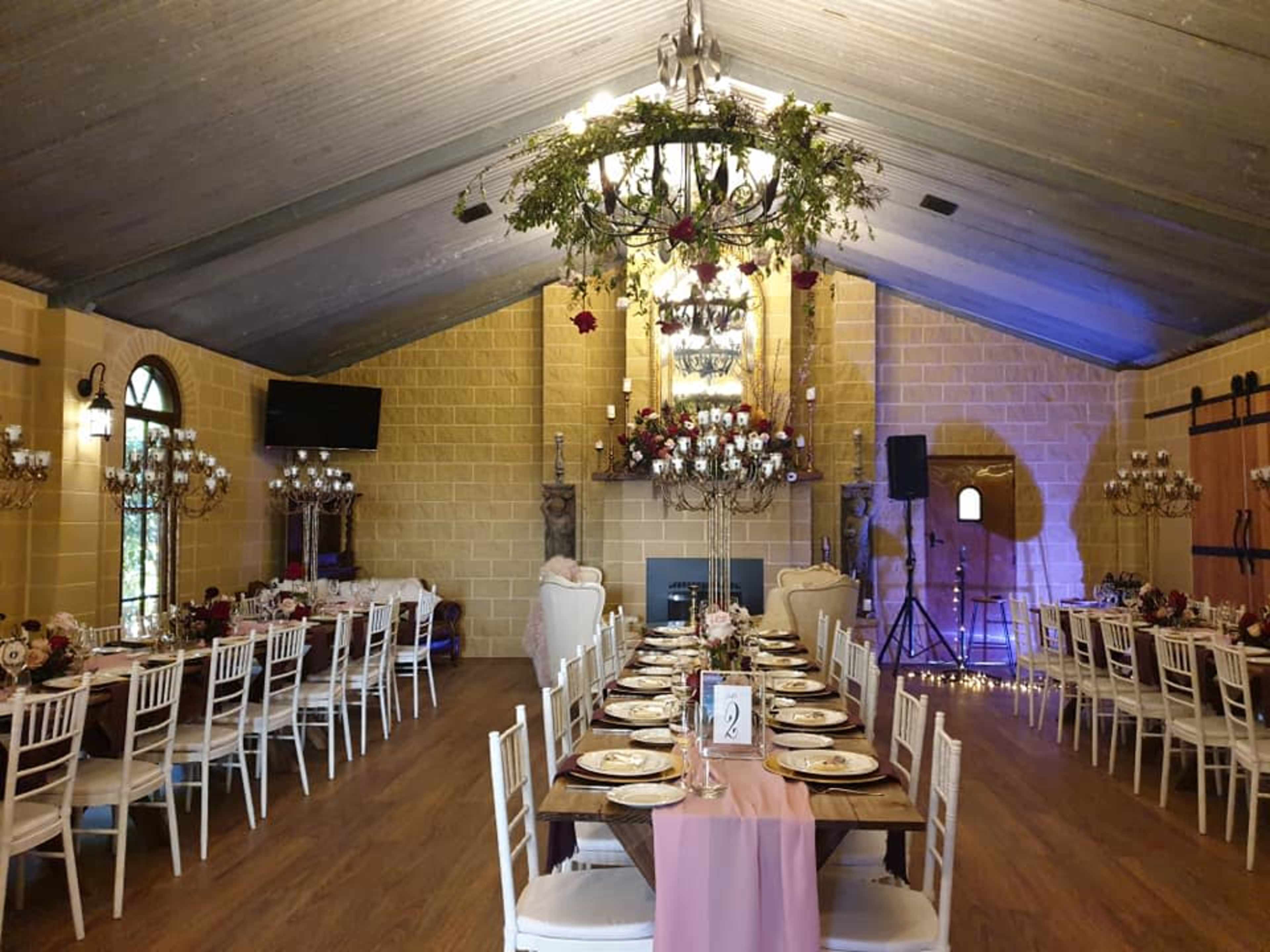 A banquet hall decorated with long tables set for dining, featuring floral centerpieces and chandeliers hanging from the vaulted ceiling.
