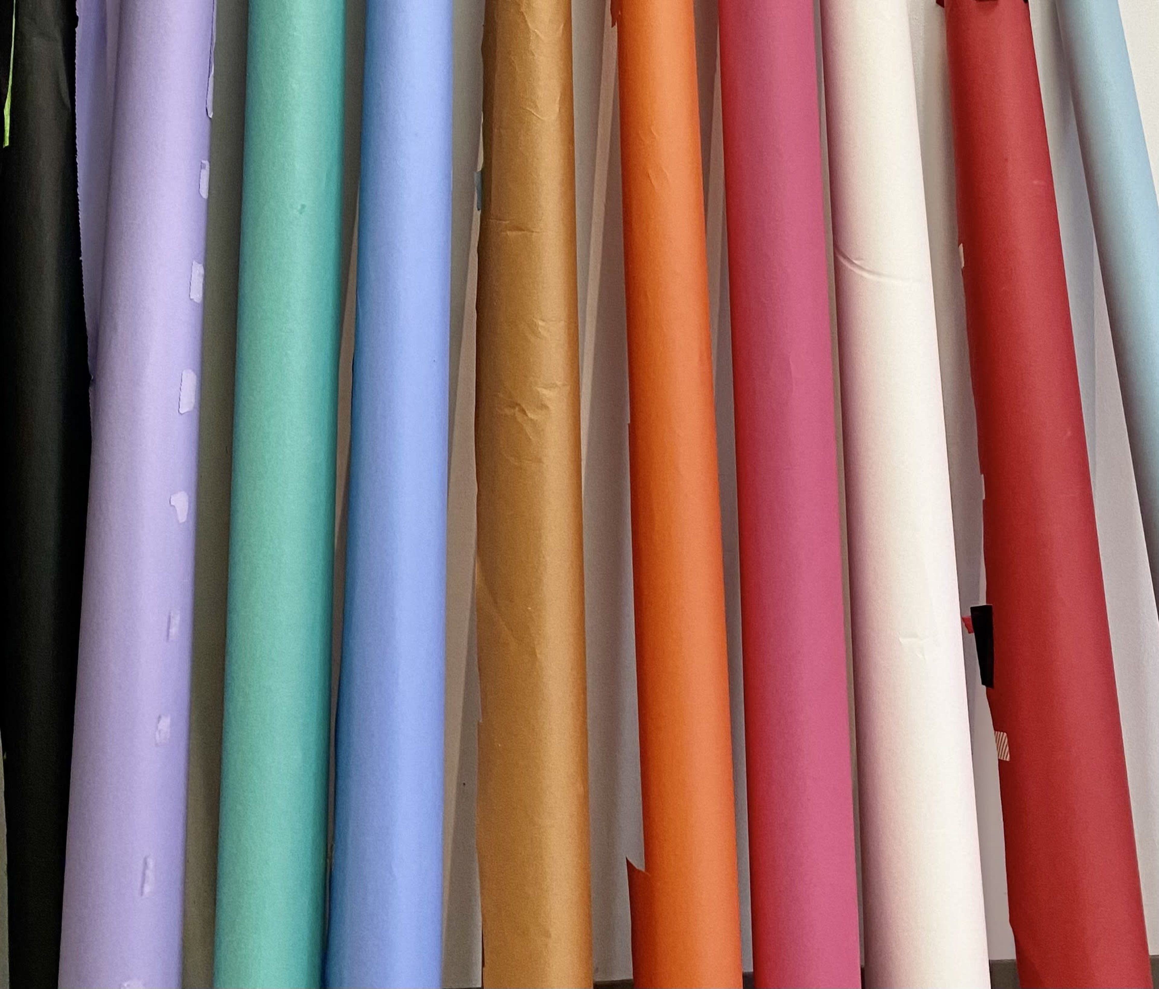 The image shows rolls of colored paper neatly arranged on a wall.