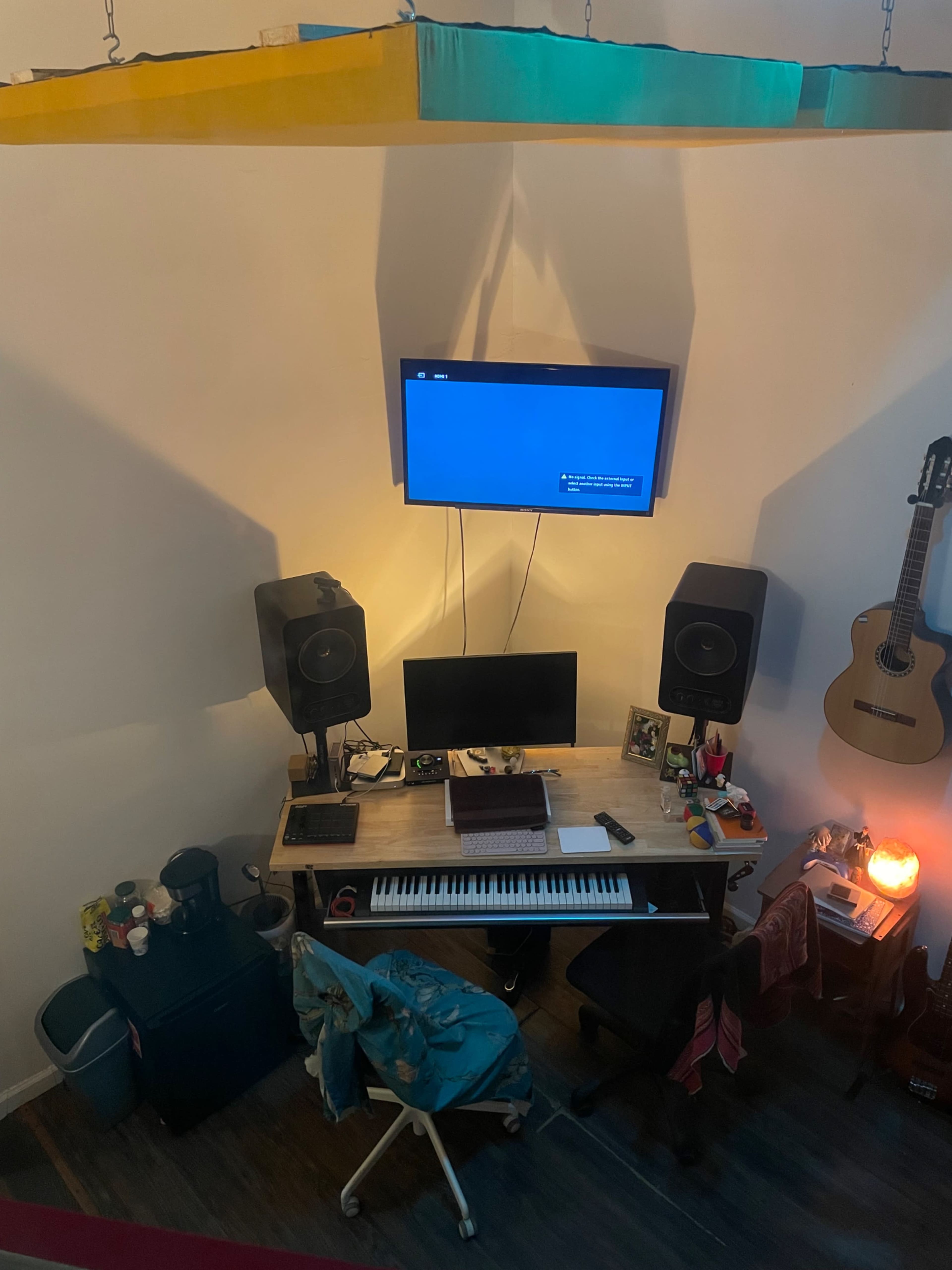 The image shows a home office setup featuring a desk with a computer, keyboard, and speakers, positioned beneath a wall-mounted television.
