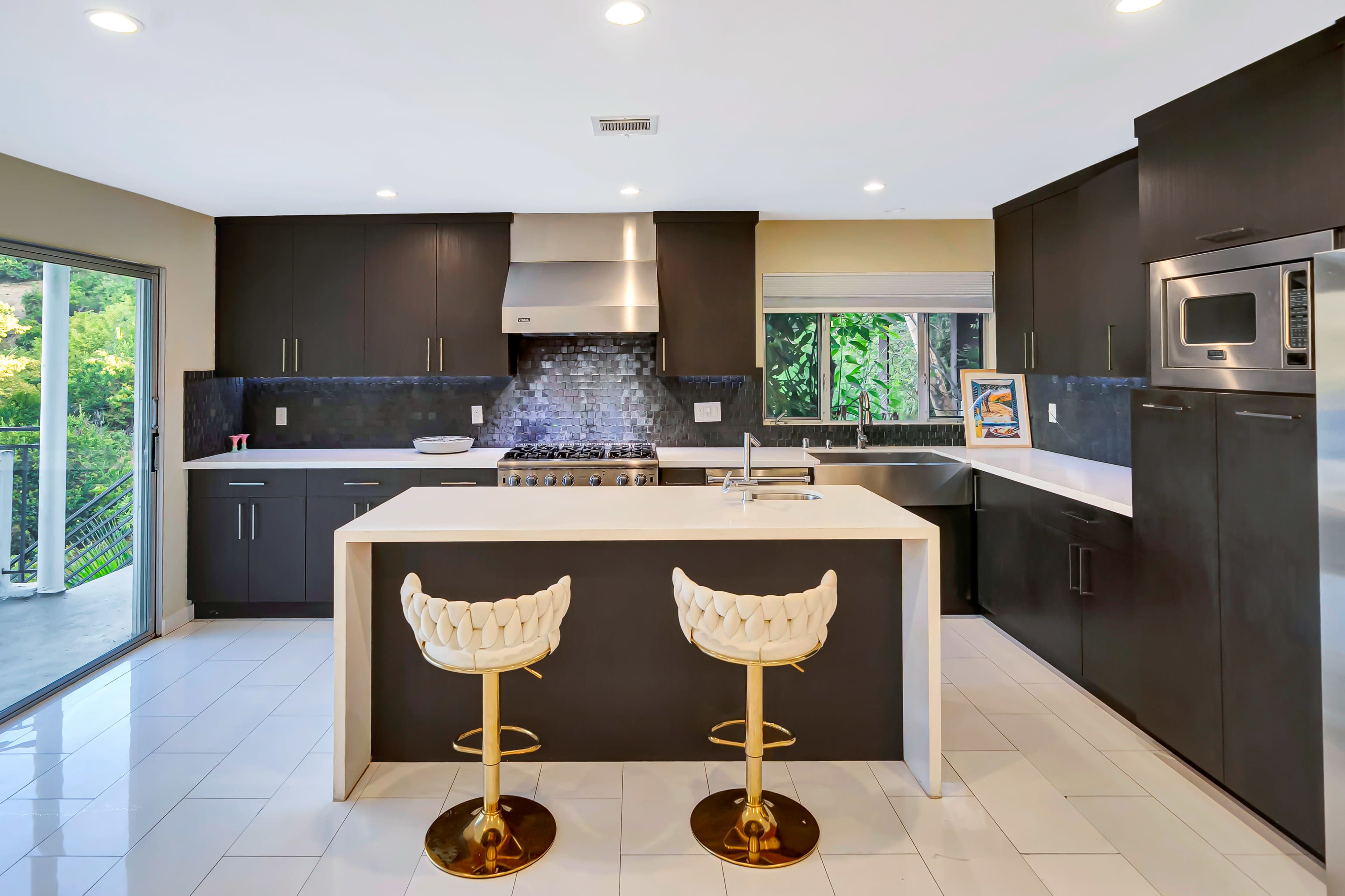 The kitchen features dark cabinetry, a central island with gold-accented stools, and stainless steel appliances.