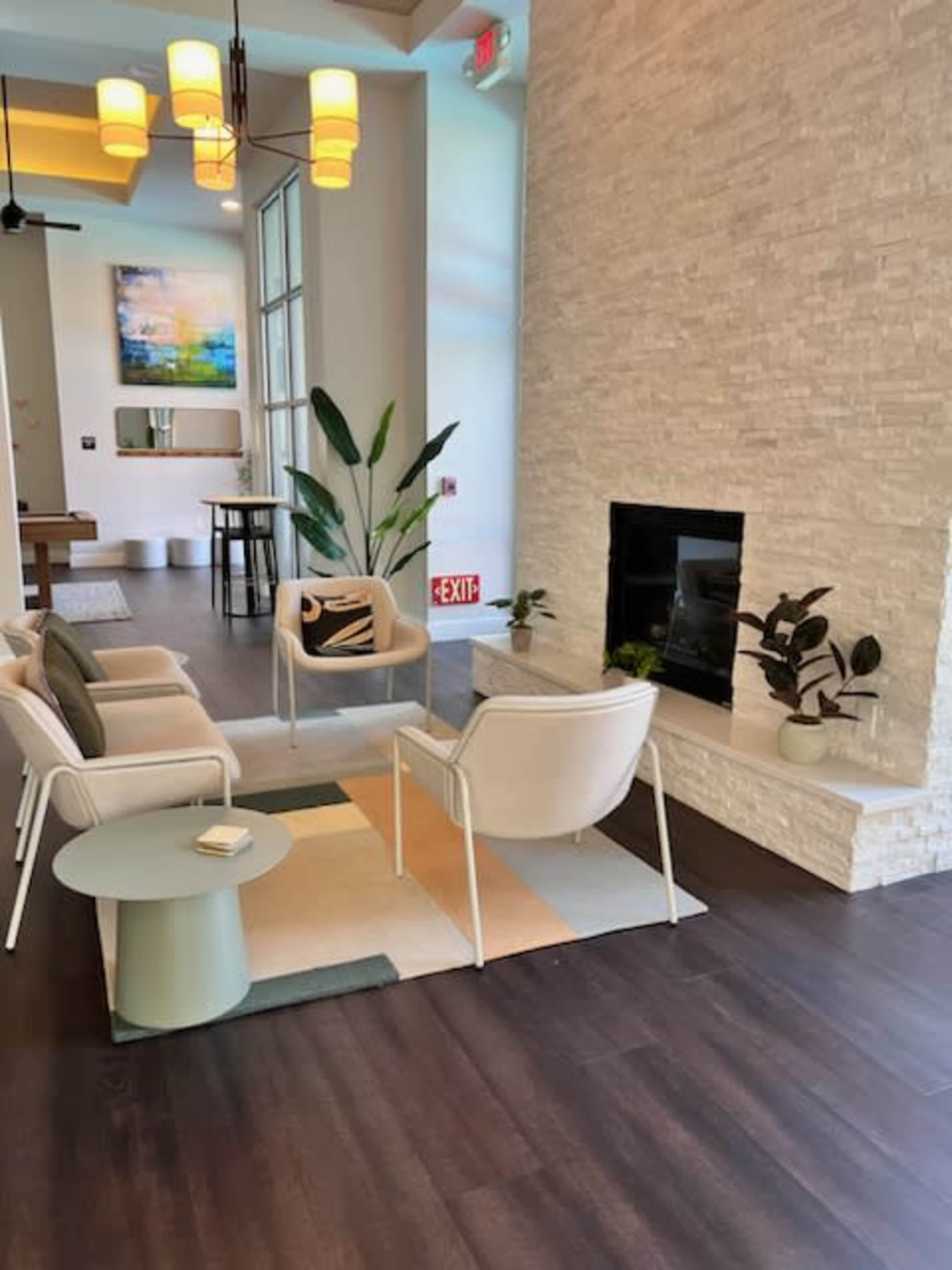 A modern seating area features white chairs around a small table, set near a stone fireplace and decorated with plants.