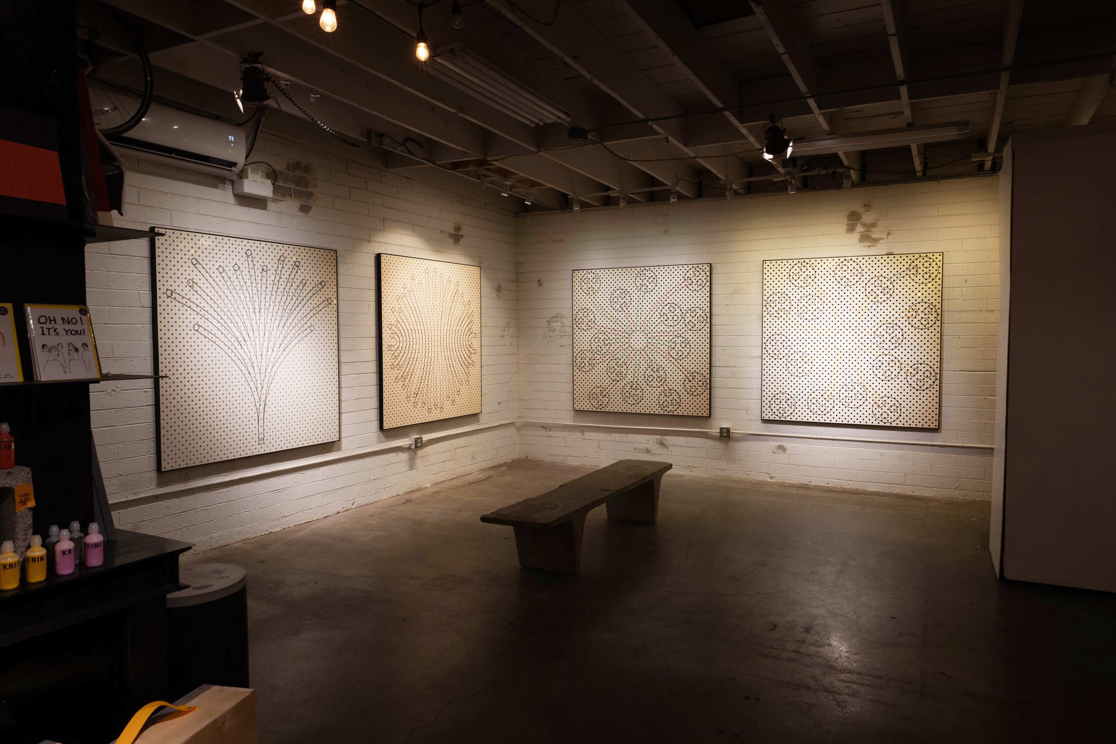 The image shows an art gallery with four framed artworks on the white brick walls and a concrete bench in the center.