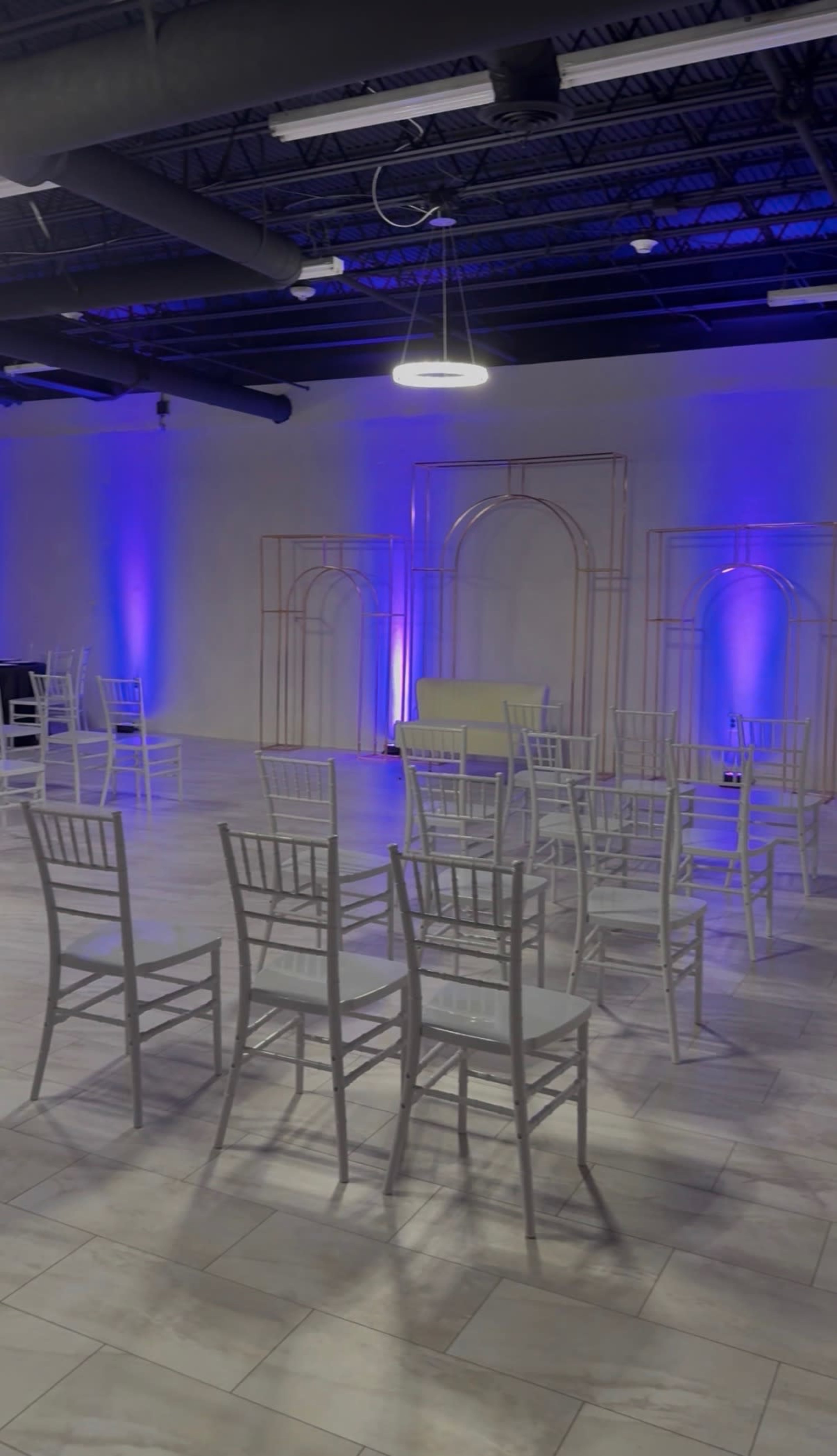 The image shows a spacious event venue arranged with white chairs facing a decorative backdrop illuminated by blue lights.