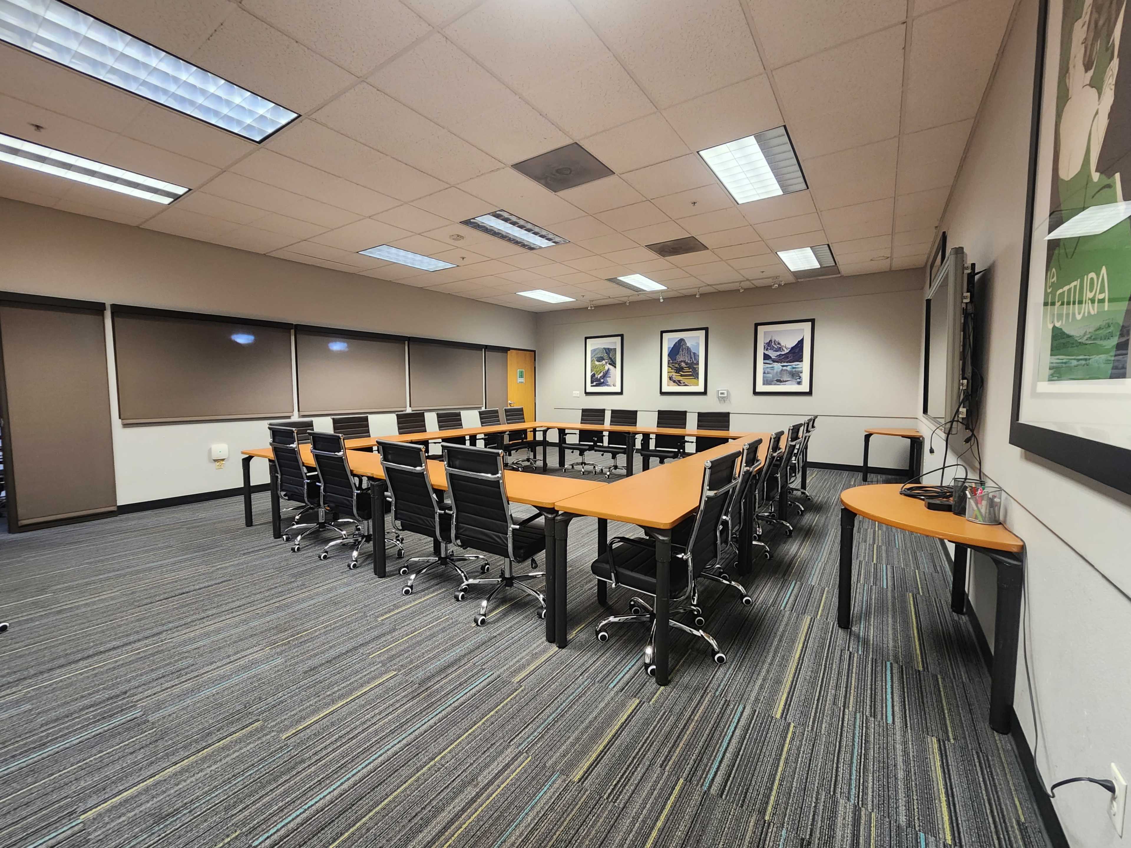 The image shows a modern conference room set with a long table surrounded by black chairs, floor-to-ceiling windows, and framed artwork on the walls.