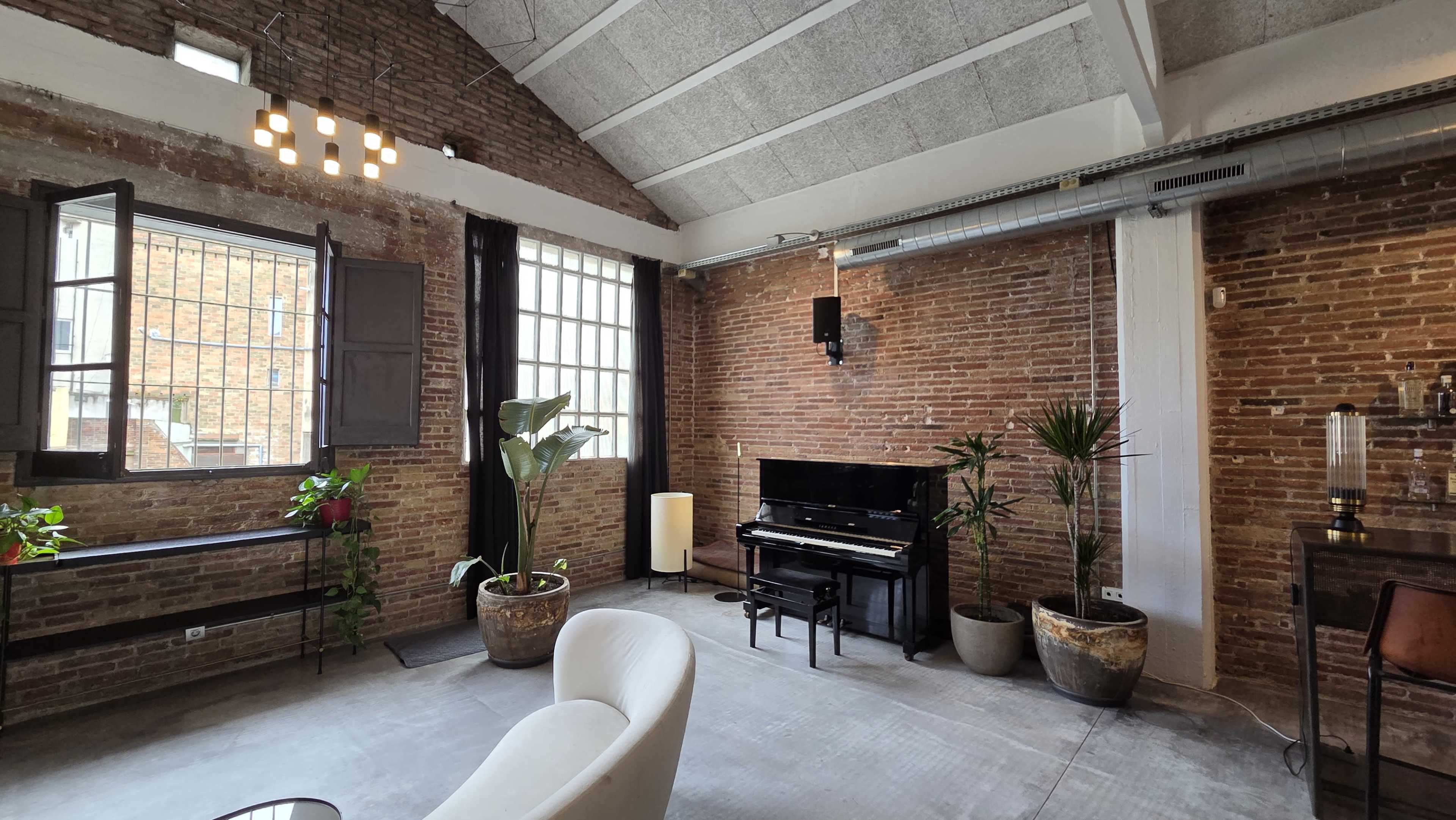 The image shows a contemporary room with brick walls, a black piano, several potted plants, and a white lounge chair.