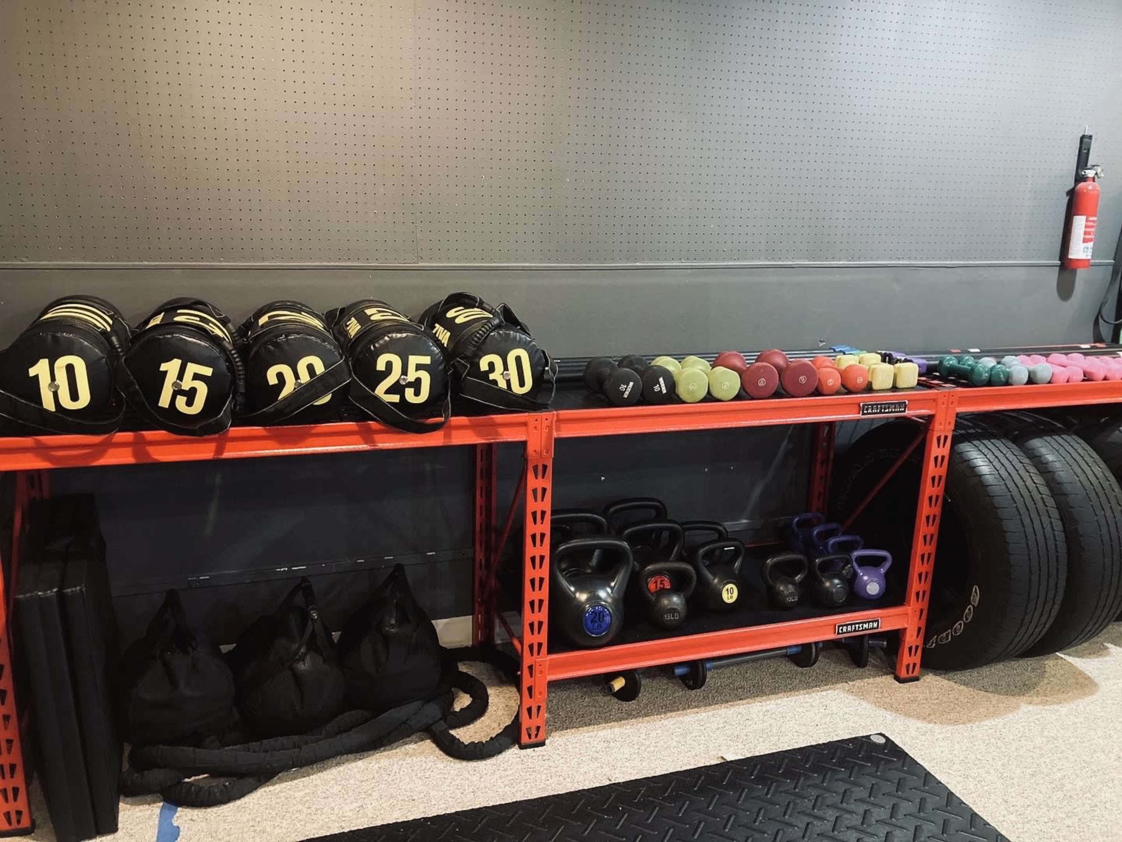 A organized gym space featuring weight plates, kettlebells, and dumbbells stored on orange shelving, alongside tires and exercise mats.