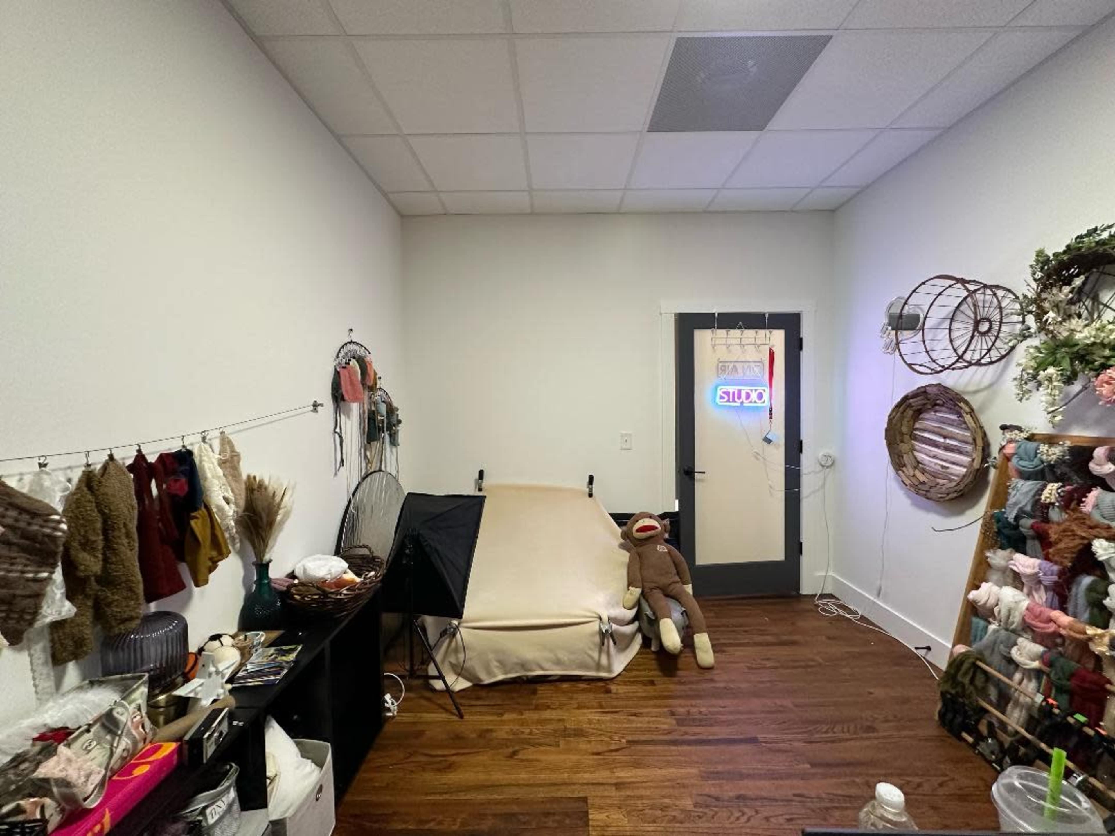 A small room with a blank wall, a bed on one side, and various decorations and items arranged on shelves and hooks.