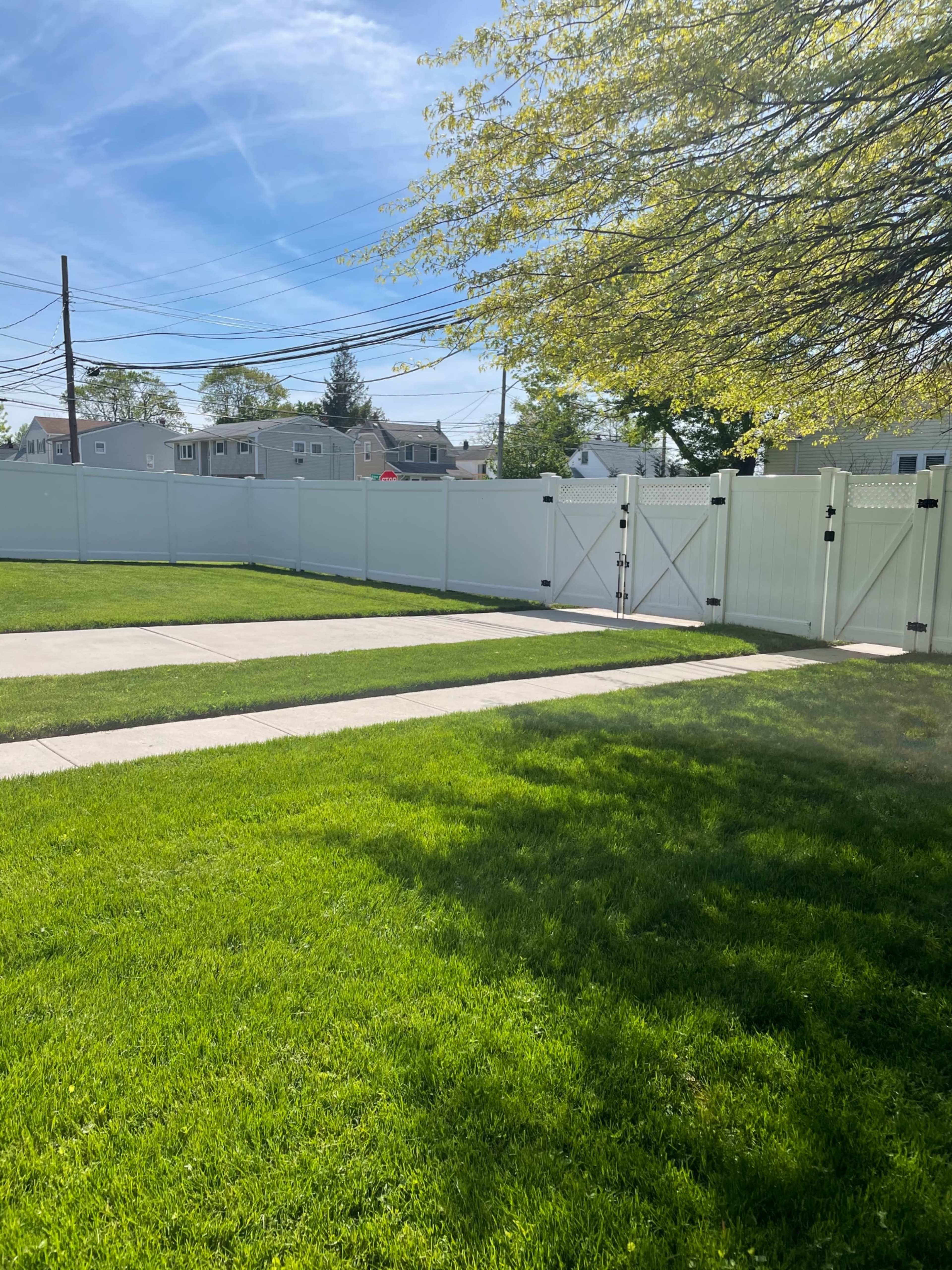 The image shows a well-maintained lawn with two paths leading to a white fence and gate under a clear blue sky.