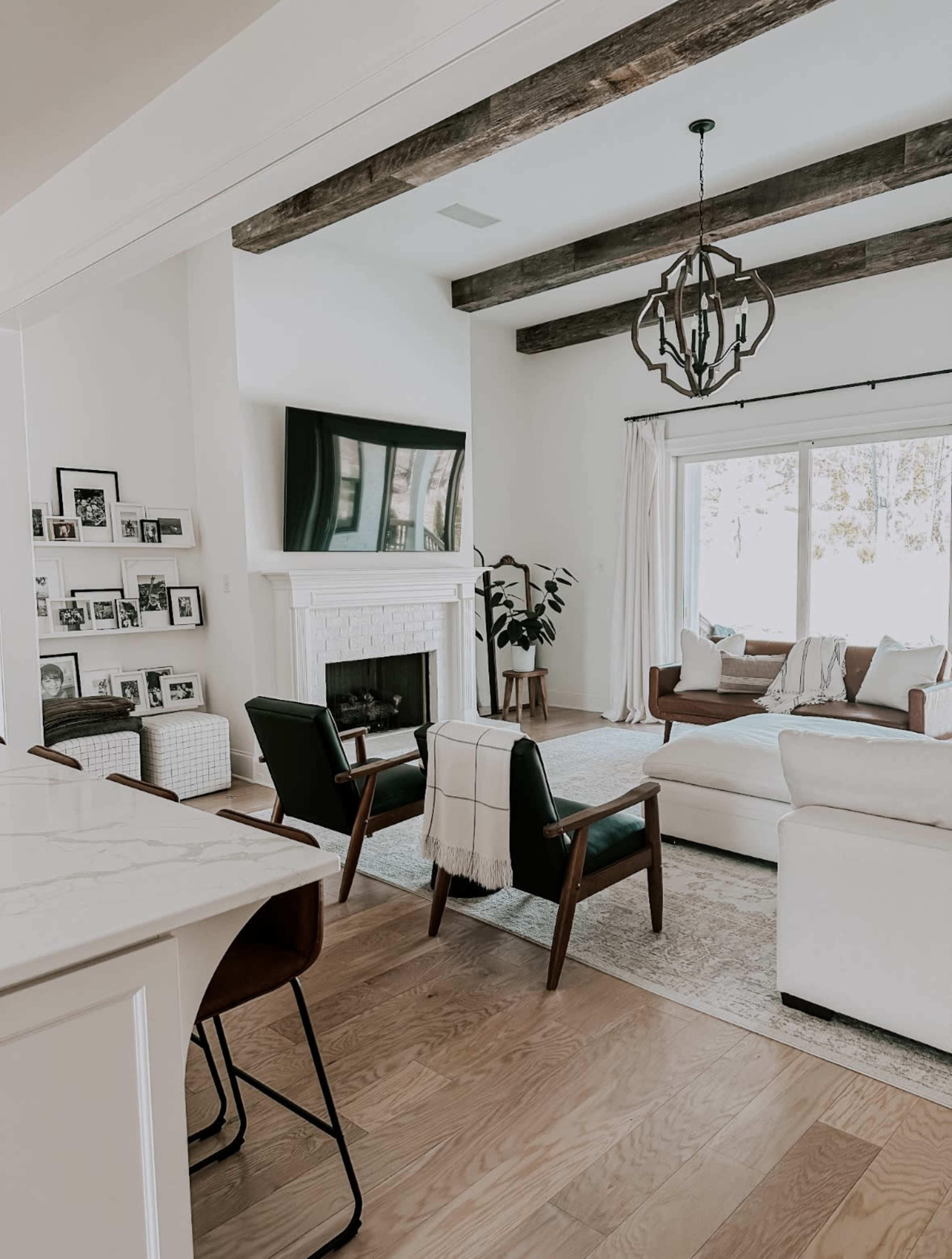 The image shows a modern living room with a fireplace, large windows, various seating options, and decorative elements.