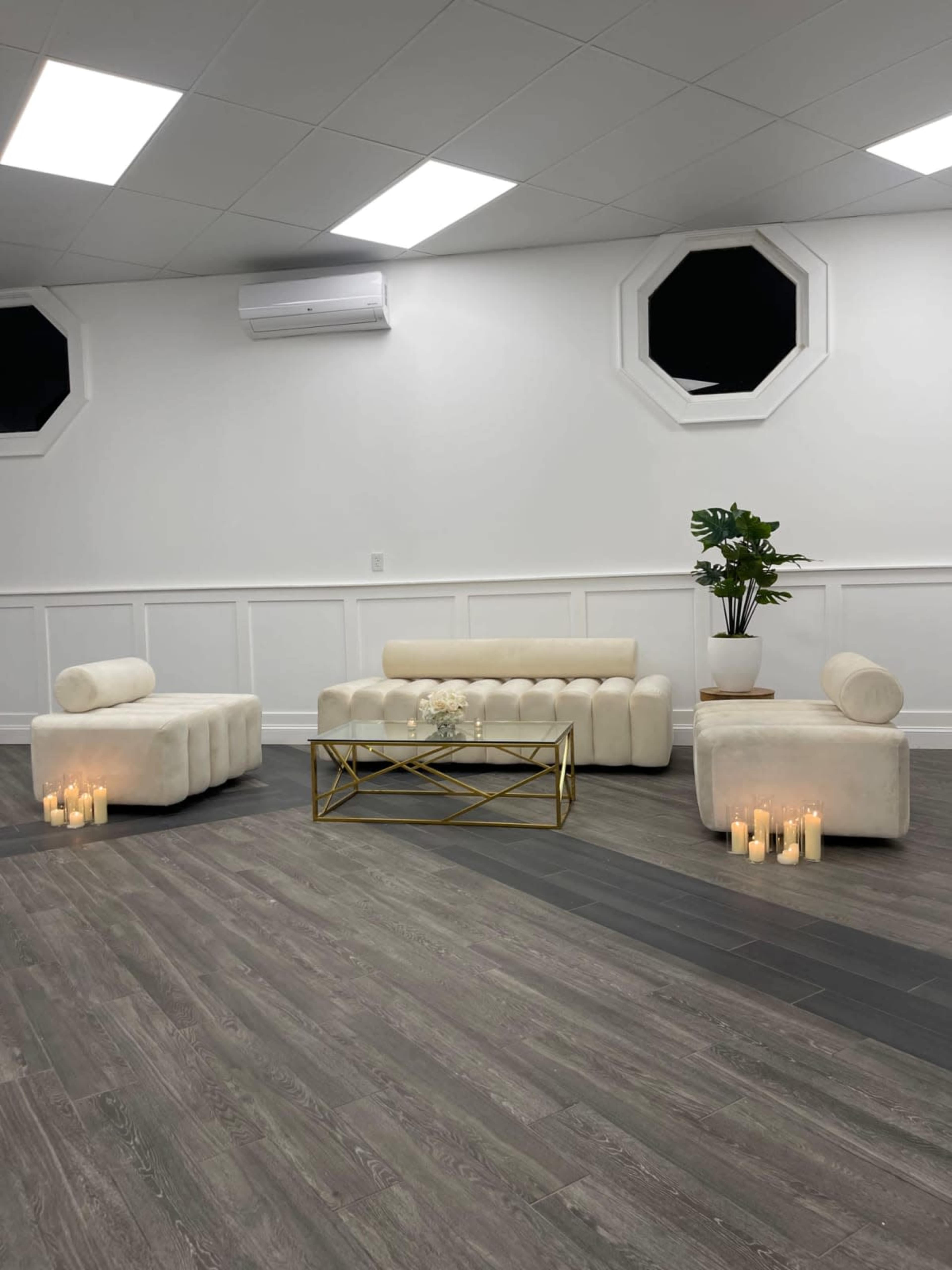 A spacious room features white seating arrangements and a gold coffee table, illuminated by candles on the floor.