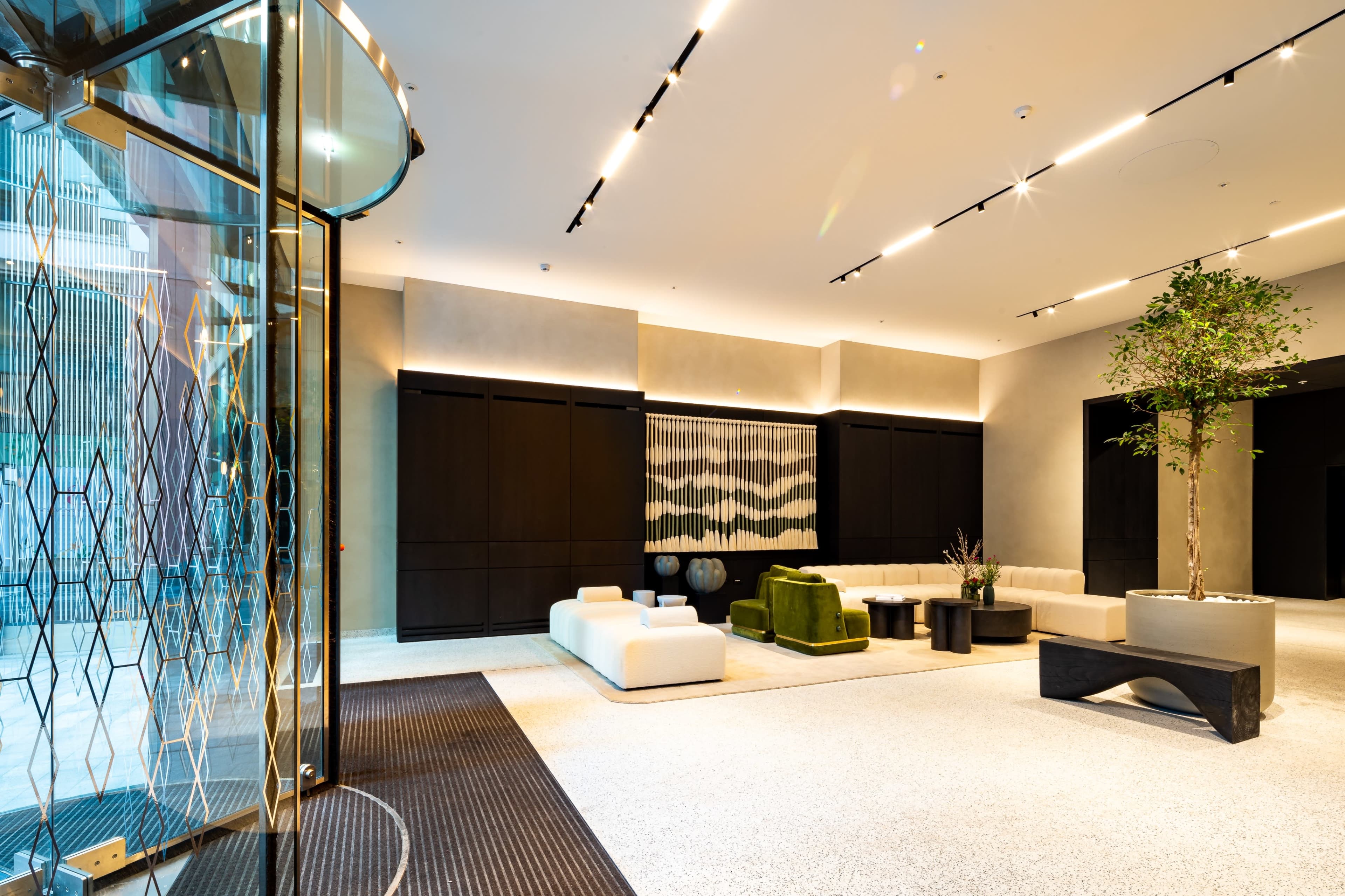 A modern lobby area featuring a combination of light and dark furnishings, with a circular glass entrance and a green accent chair next to a potted tree.