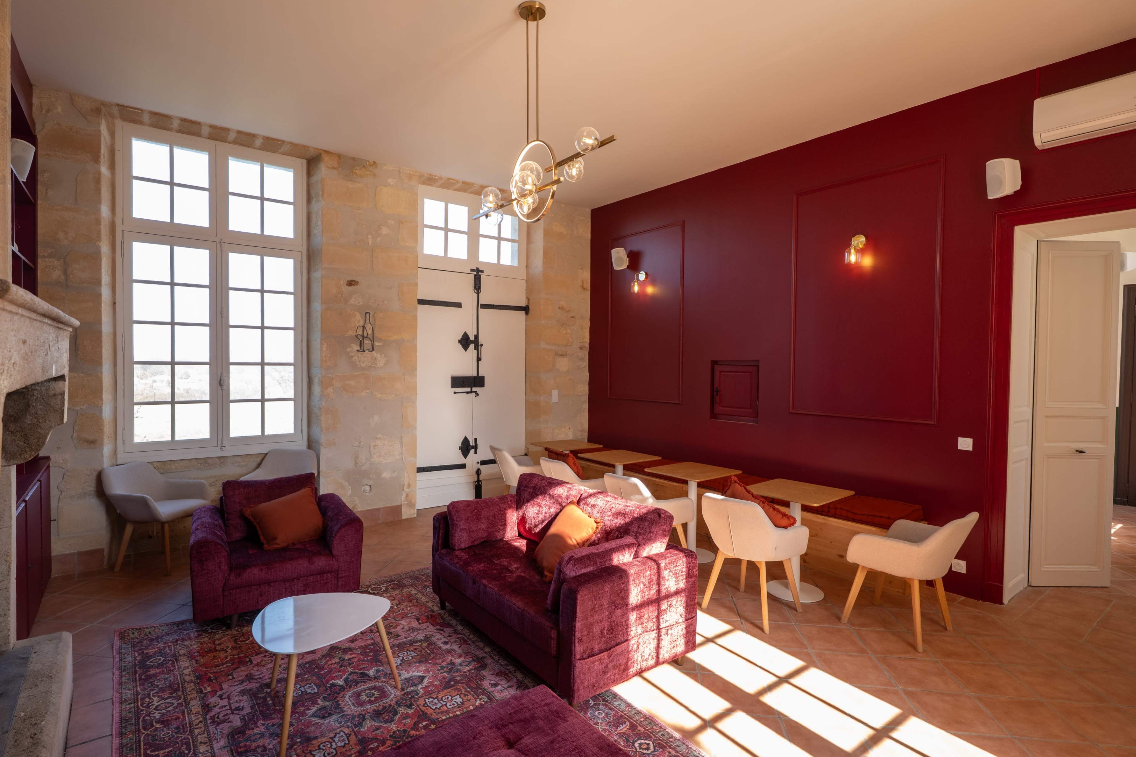 The image shows a modern living space with burgundy walls, a stone fireplace, and a mix of seating arrangements, including plush sofas and dining tables.