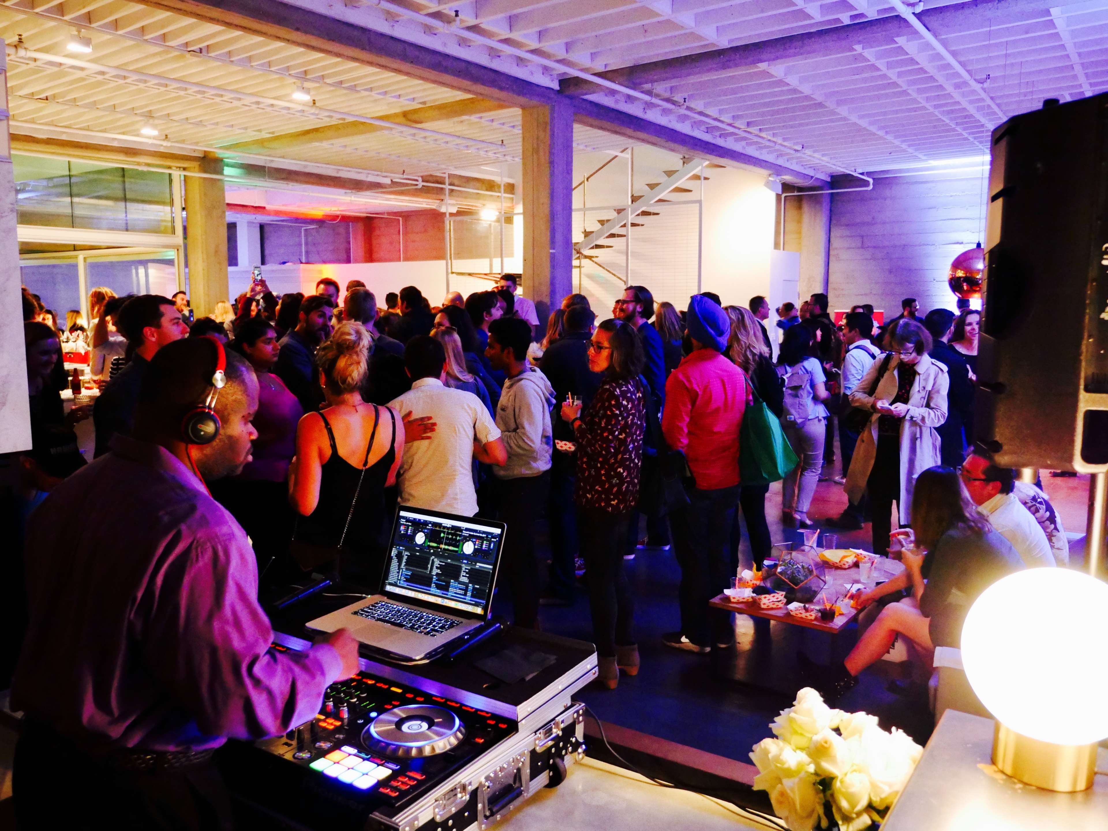 A DJ controls the music at a lively gathering filled with guests mingling in a well-lit space.