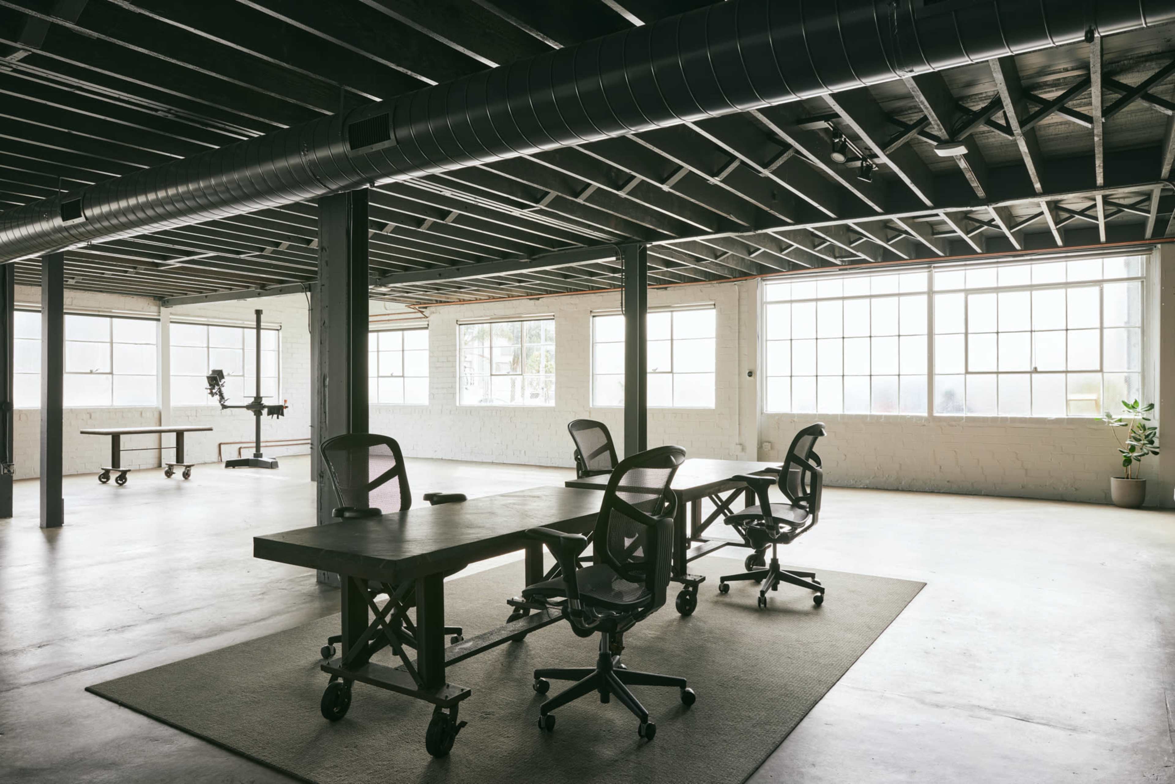 A spacious office features several workstations with rolling chairs and large windows allowing ample natural light.