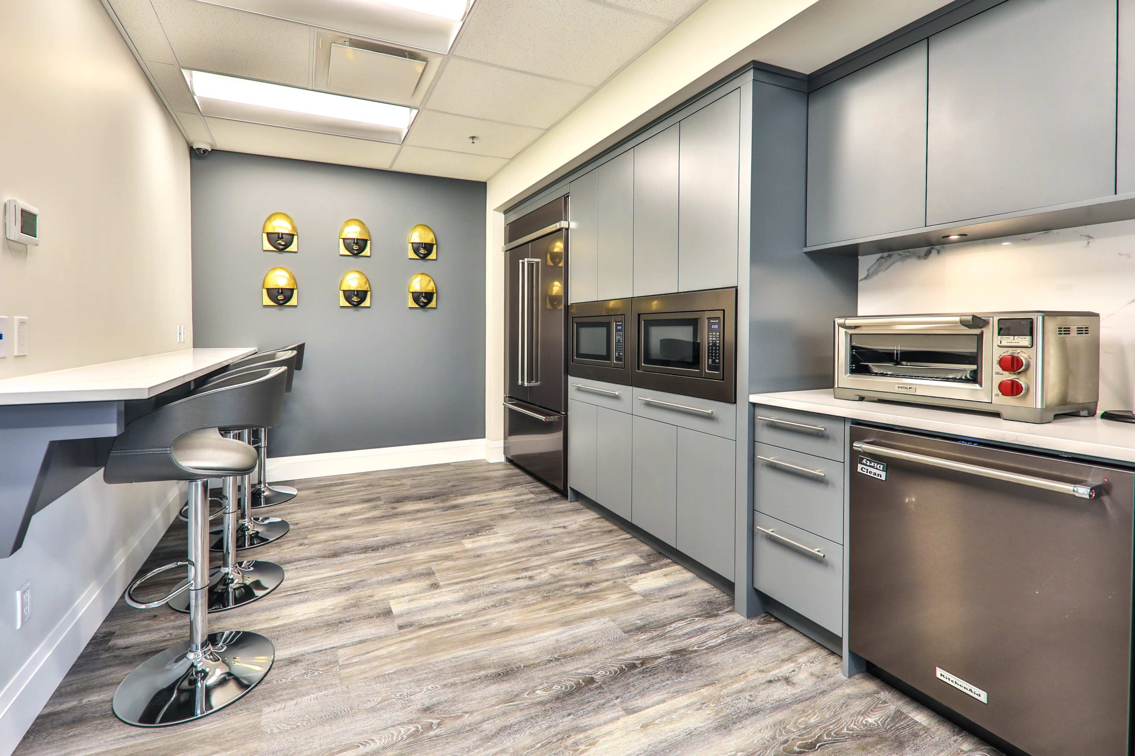 A modern kitchen with gray cabinetry, stainless steel appliances, and a sleek countertop, featuring a bar area with high stools.