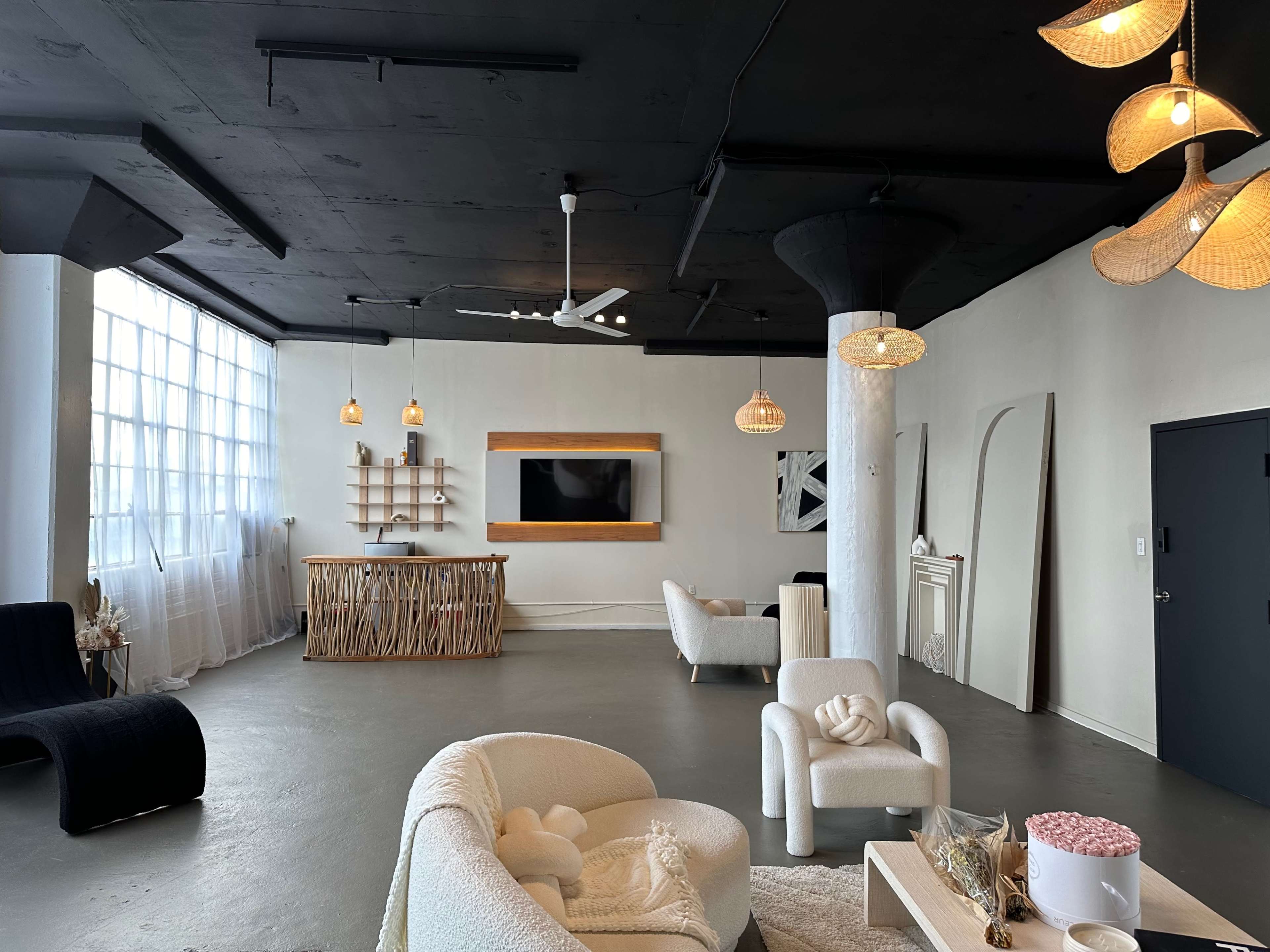 The image shows a modern, spacious interior with minimalist furniture, a large window, and various hanging light fixtures.