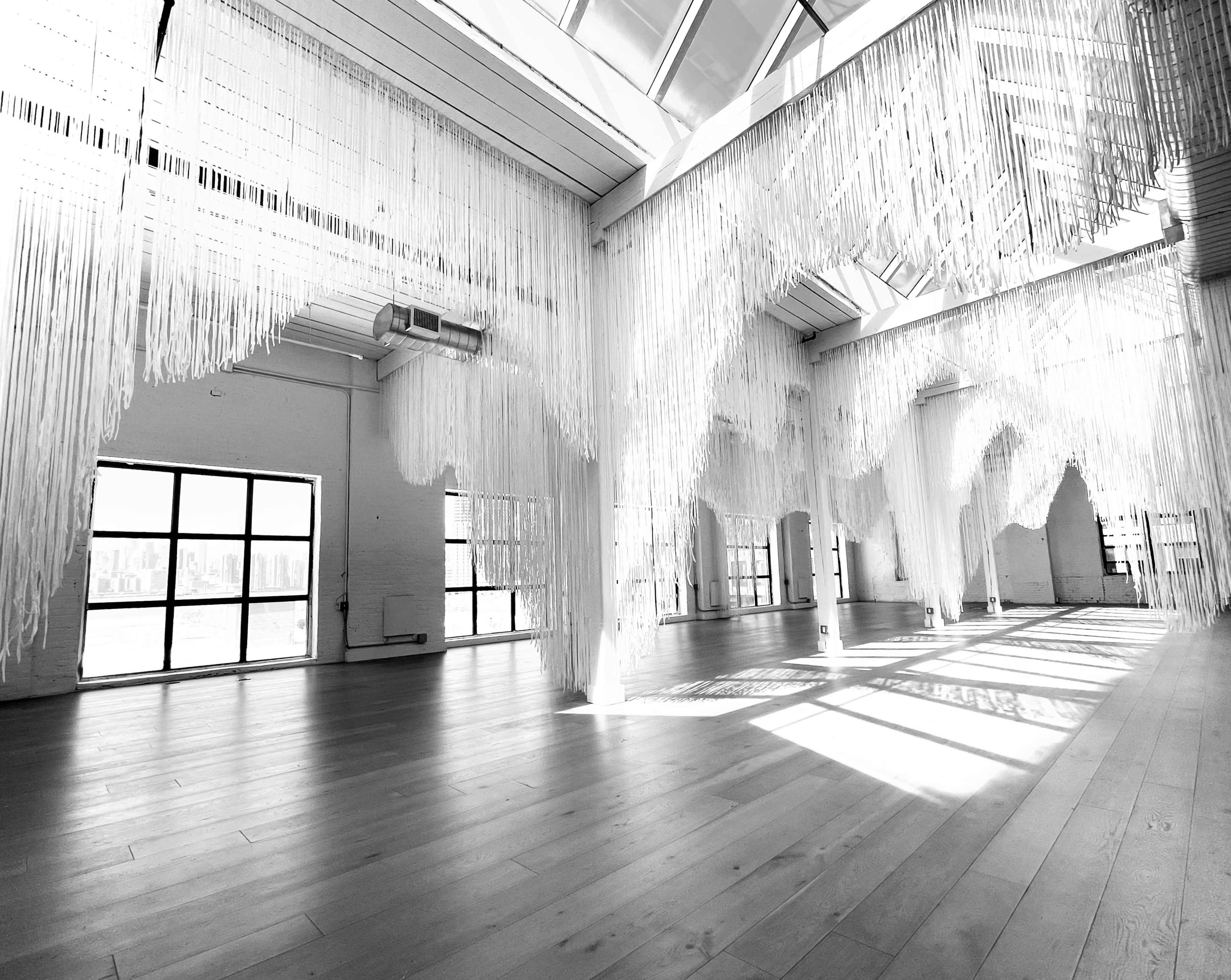 The interior of a spacious room features cascading white strands hanging from the ceiling, with large windows allowing natural light to flood in.