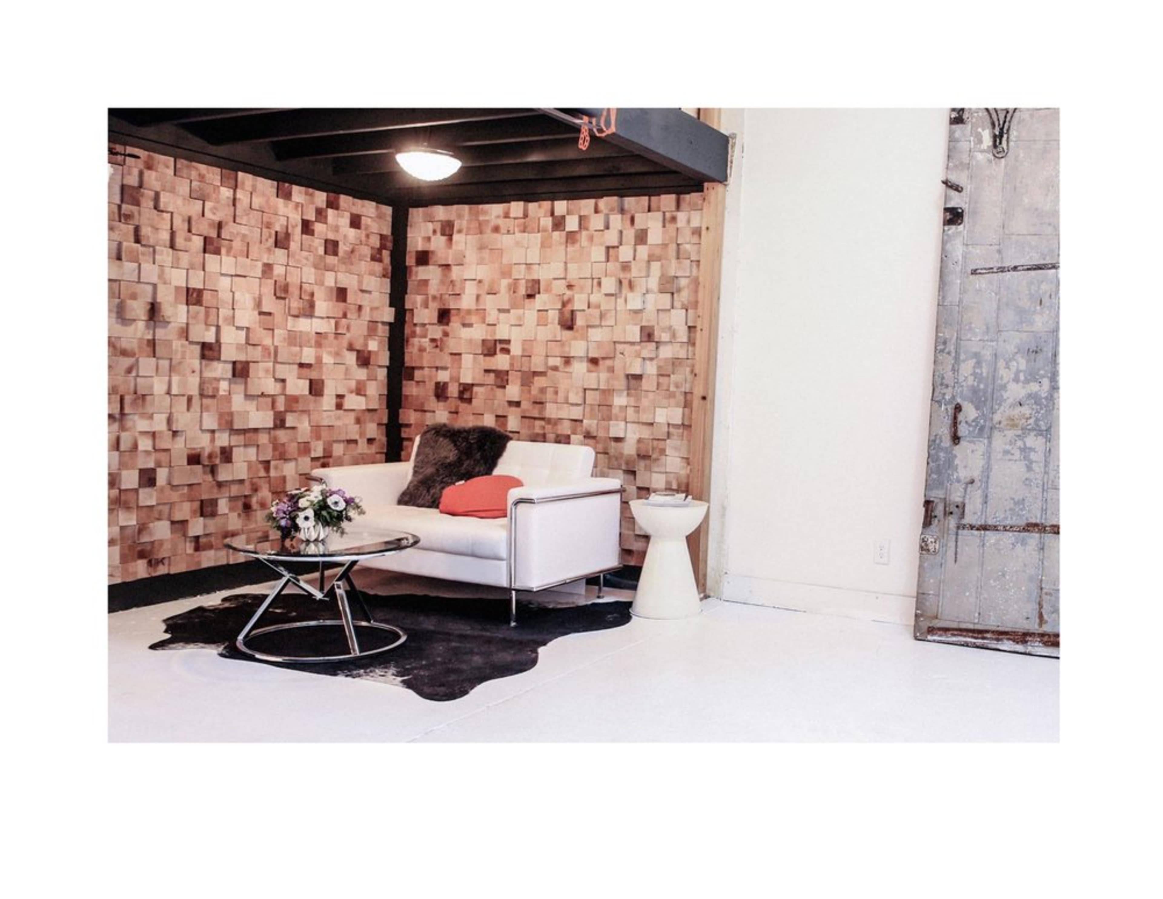A white couch with a red throw pillow and a fur accent rests on a black and white rug in a room with wooden block walls and a vintage door.