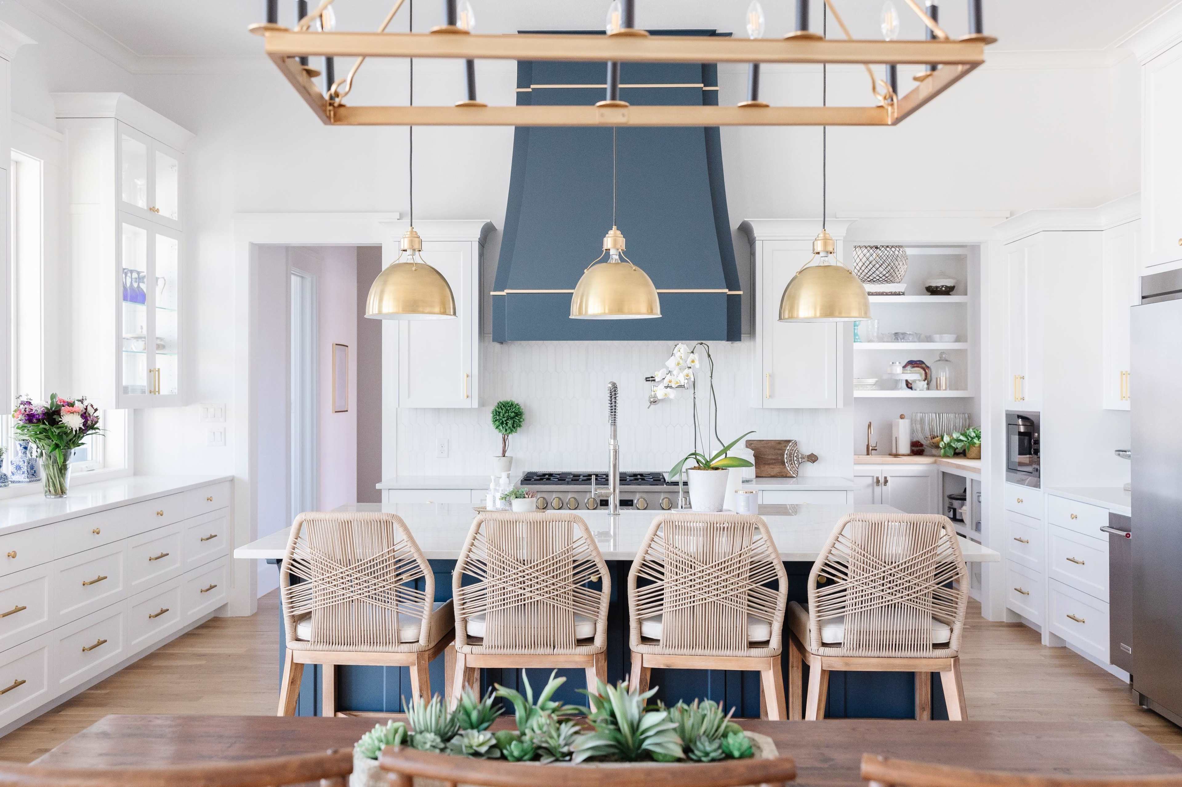 A modern kitchen features a large island with a gas stove, surrounded by six wooden seats and pendant lights above.