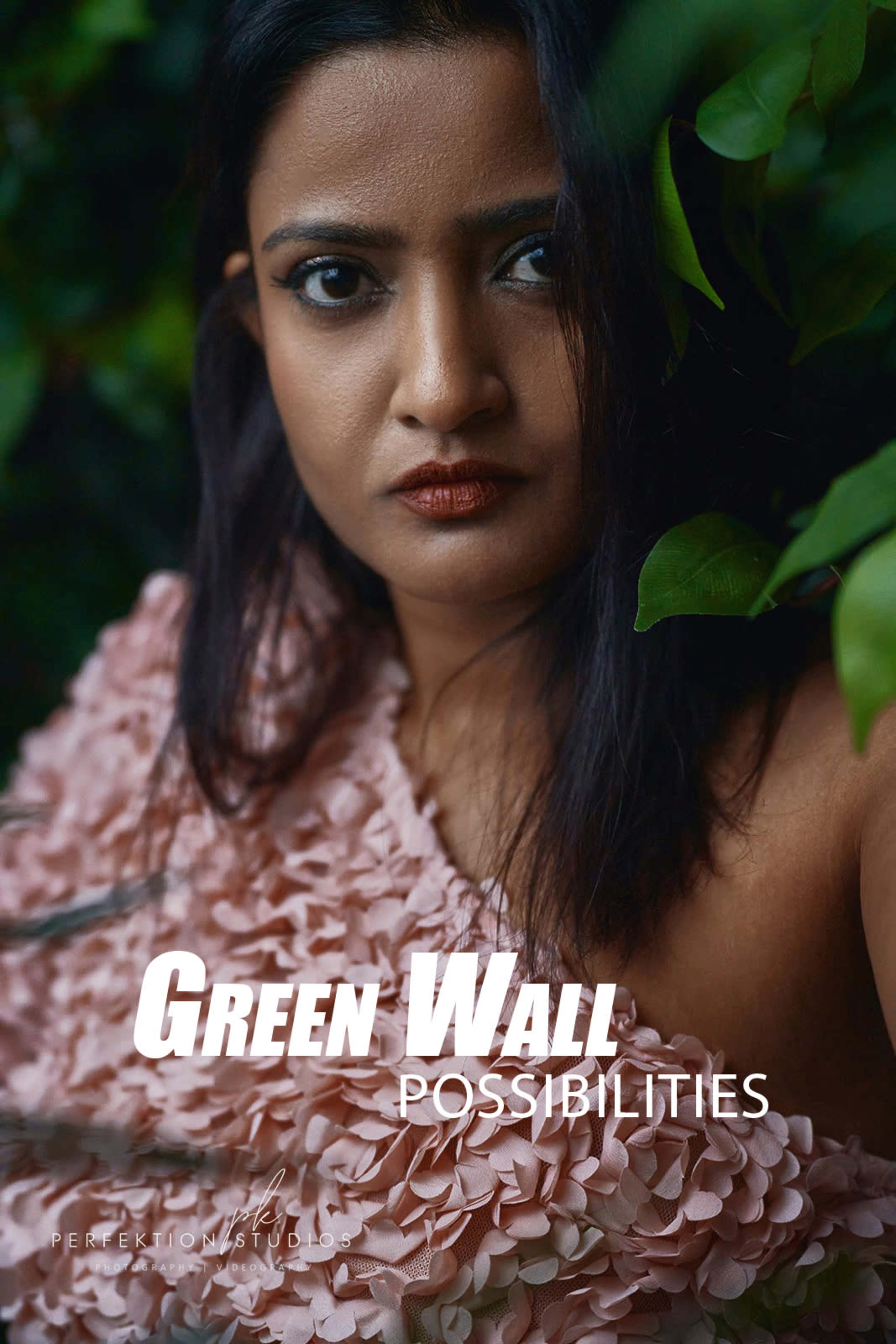 A person with dark hair poses in front of a green wall, wearing a textured pink garment.