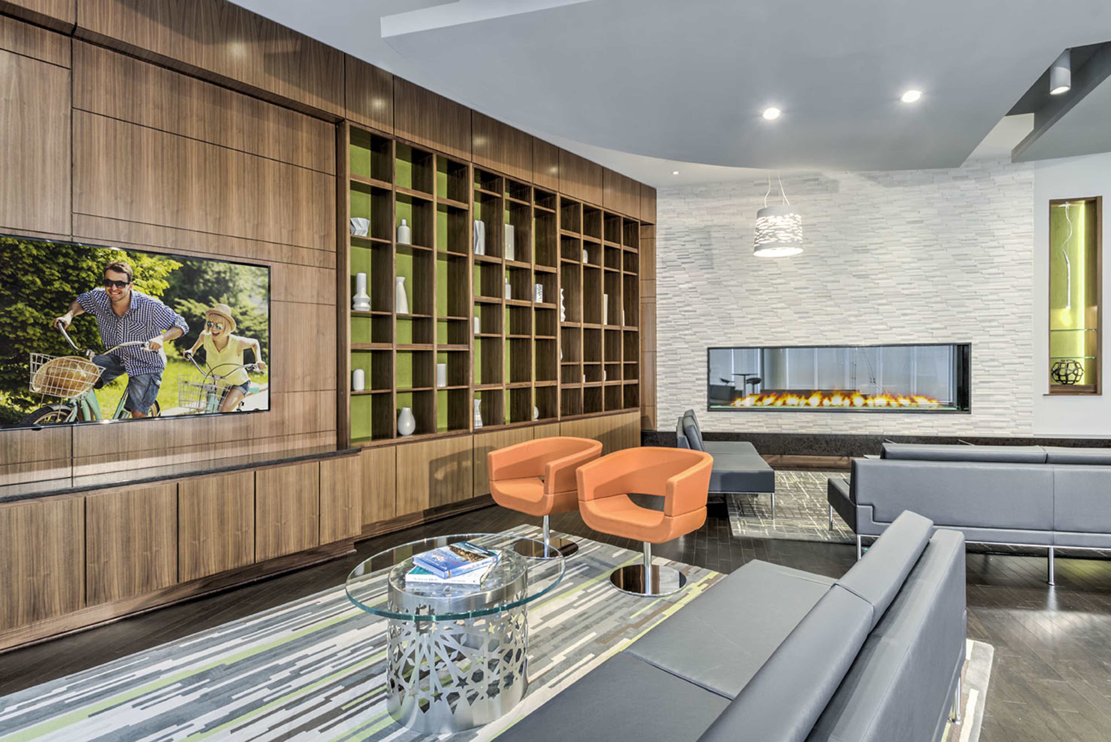 A modern living area with a curved wooden wall, a flat-screen TV, an enclosed fireplace, and contemporary furniture including orange chairs and a glass coffee table.