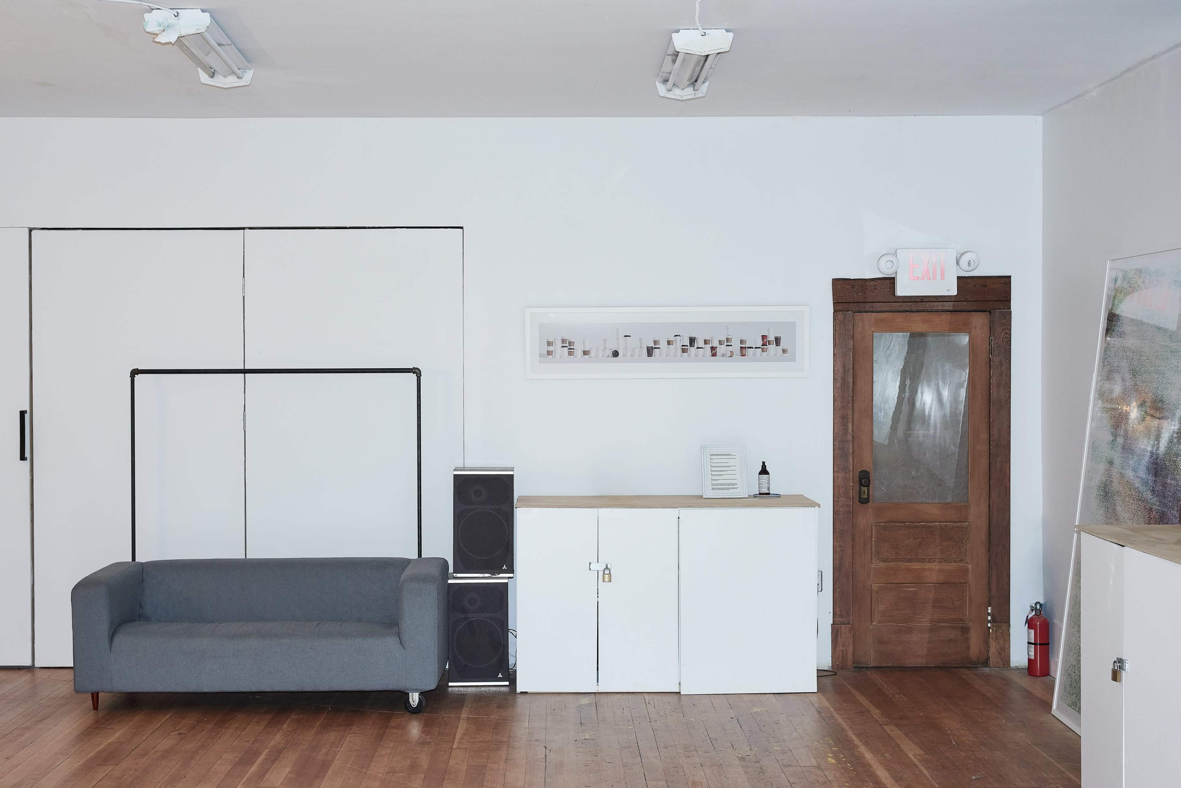 A minimalist room with a gray couch, a wooden door, a cabinet, and a framed artwork on the wall.