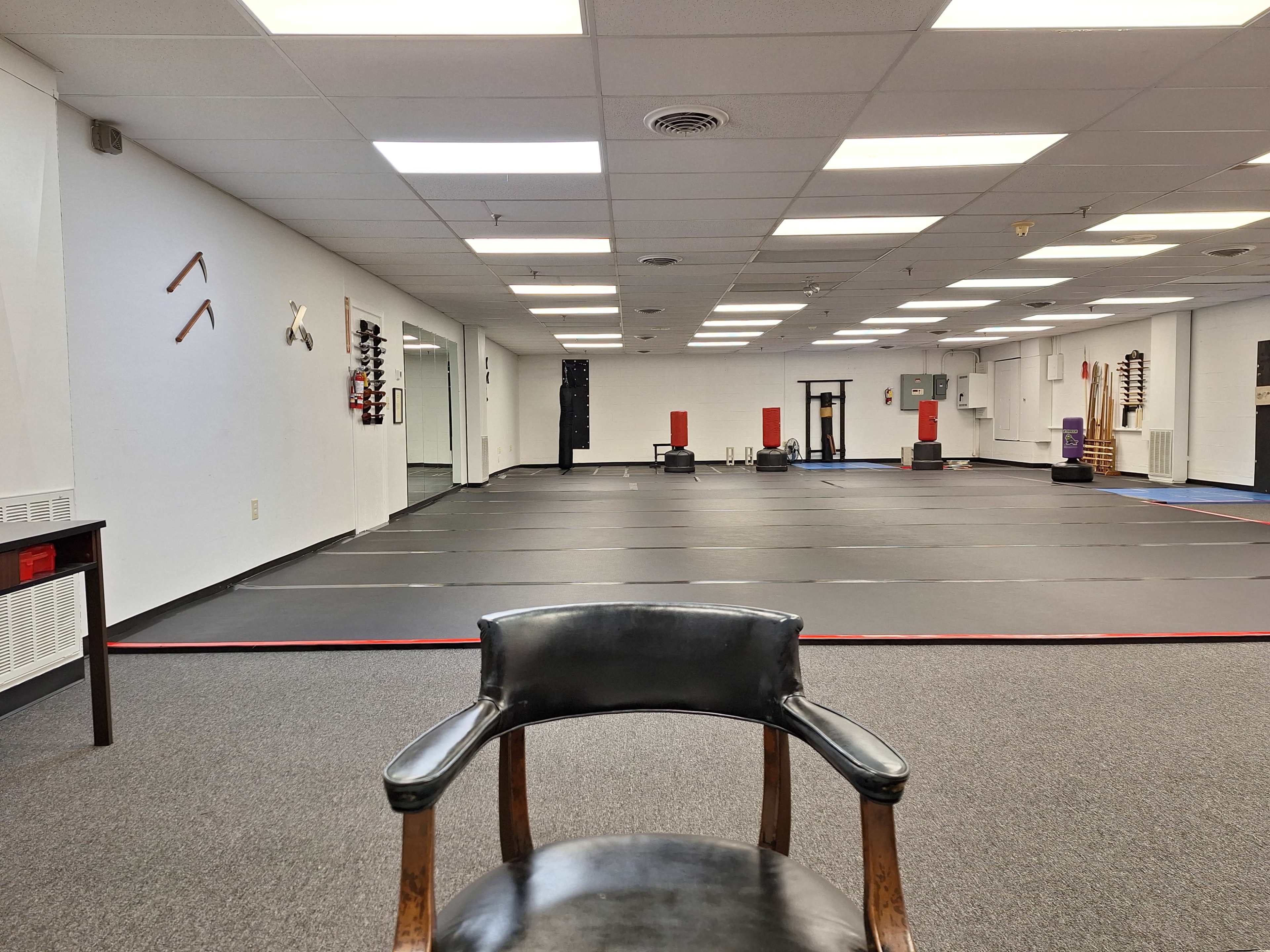 The image shows the interior of a martial arts training facility with mats laid out on the floor and equipment displayed on the walls.