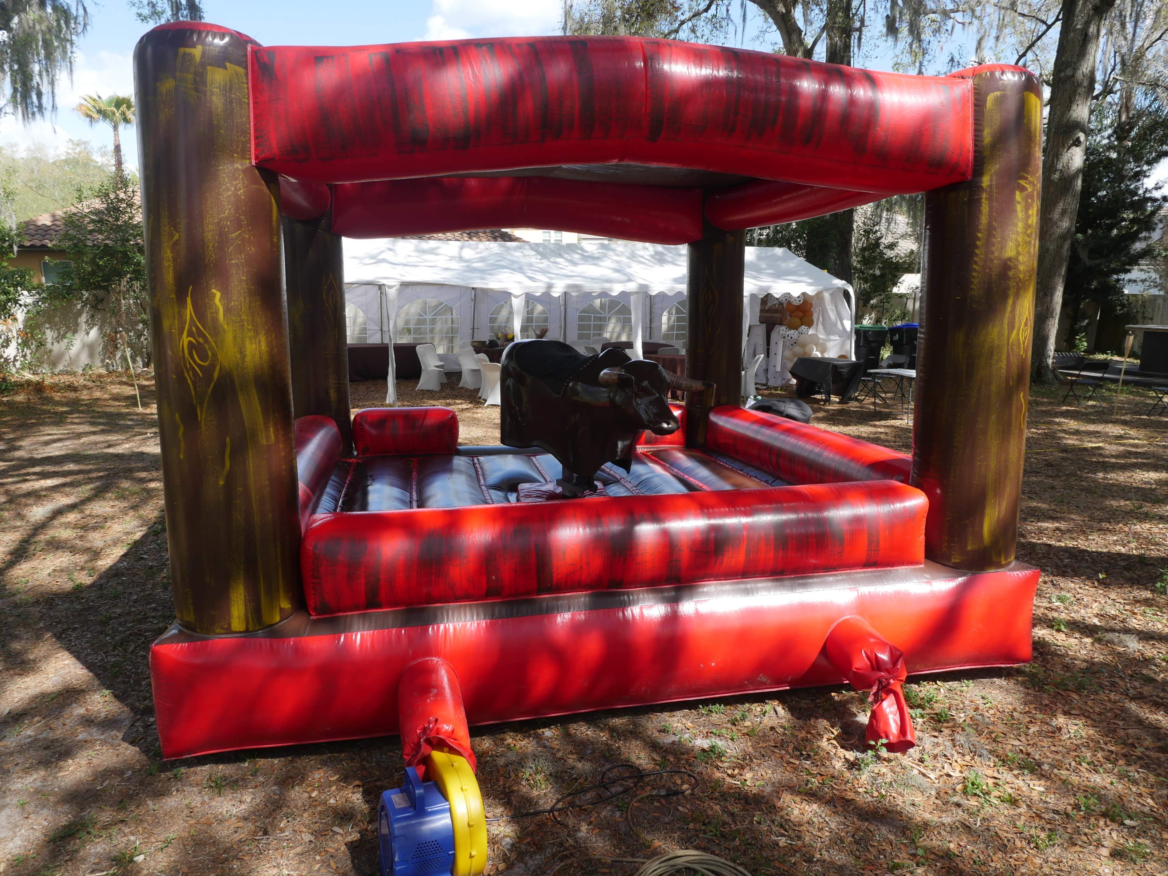 A mechanical bull is situated inside a colorful inflatable ring at an outdoor event space.