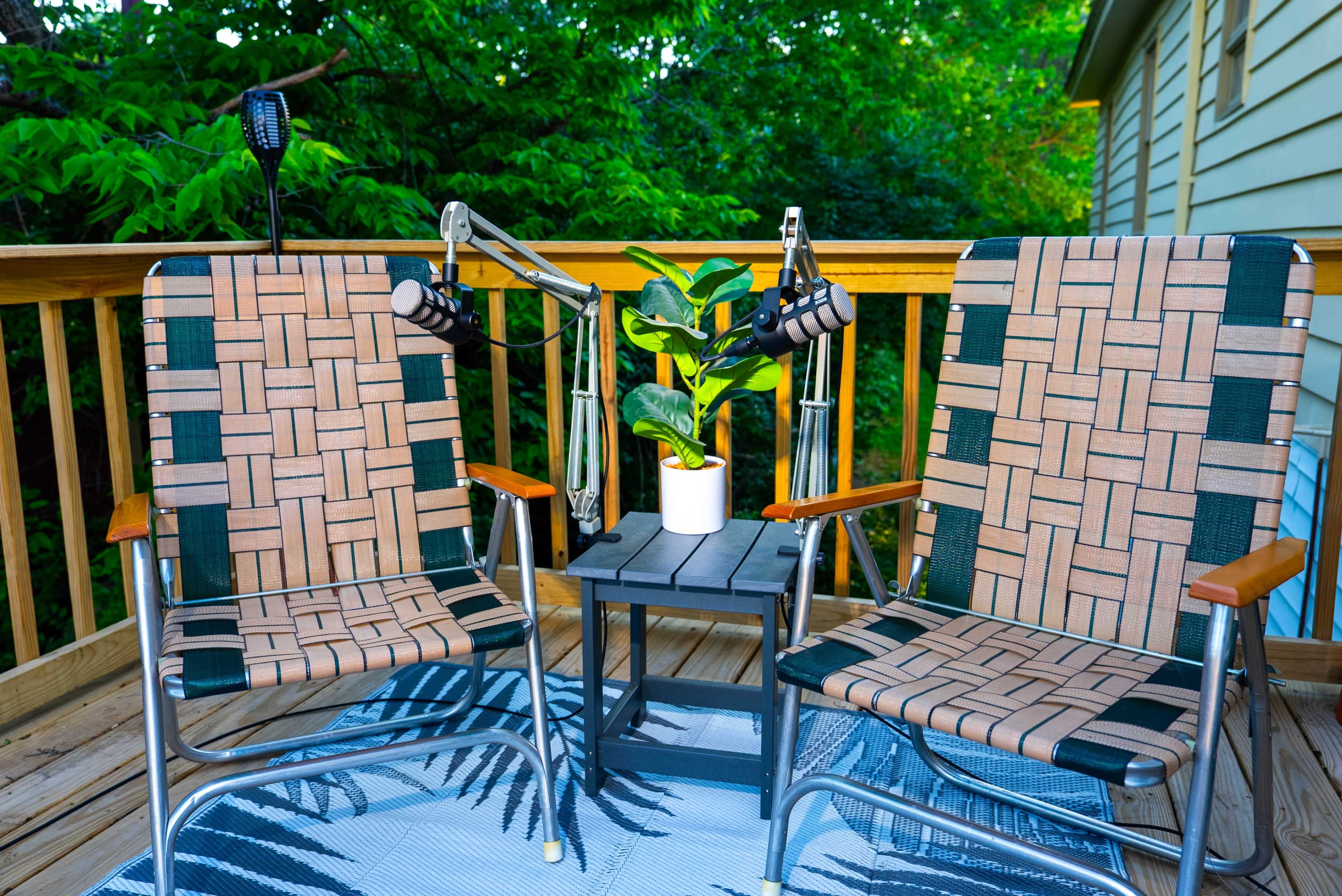 Two woven lounge chairs sit on a wooden deck beside a small black table holding a potted plant.