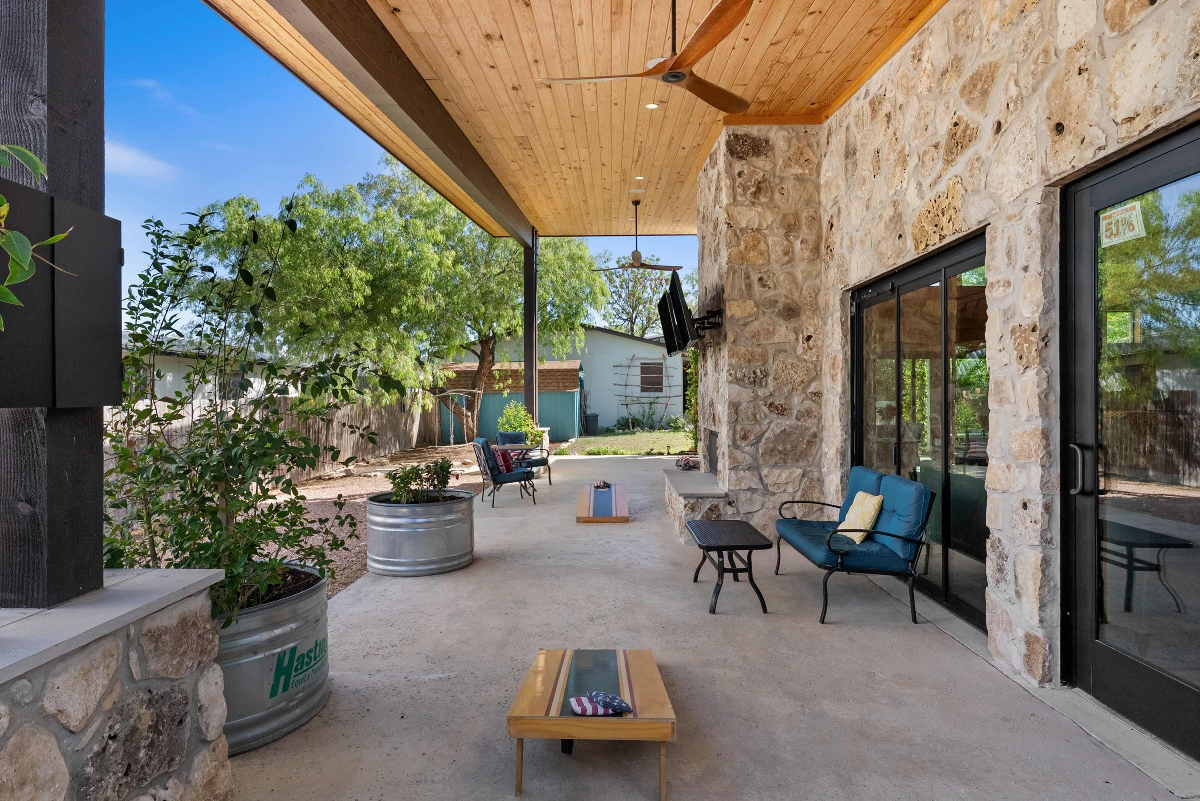 A covered patio features stone walls, a wooden ceiling, outdoor seating, and potted plants.