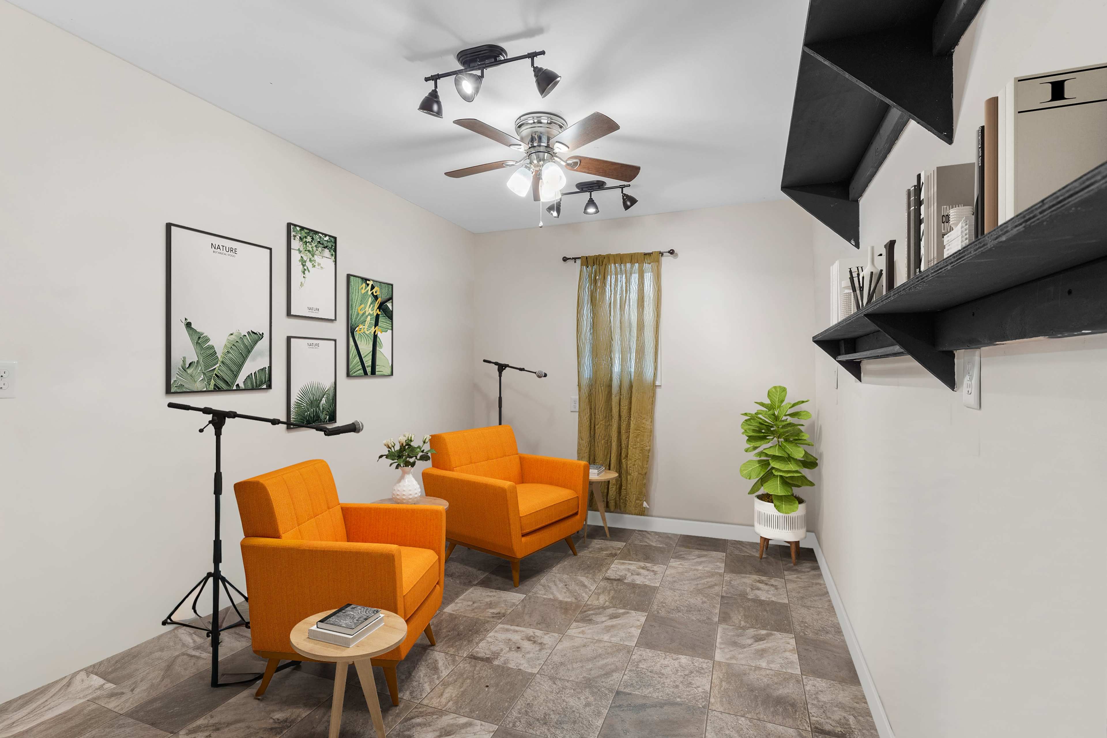 The image shows a room with two orange armchairs, a small plant, wall-mounted shelves, and framed pictures, illuminated by a ceiling fan and natural light from a window.