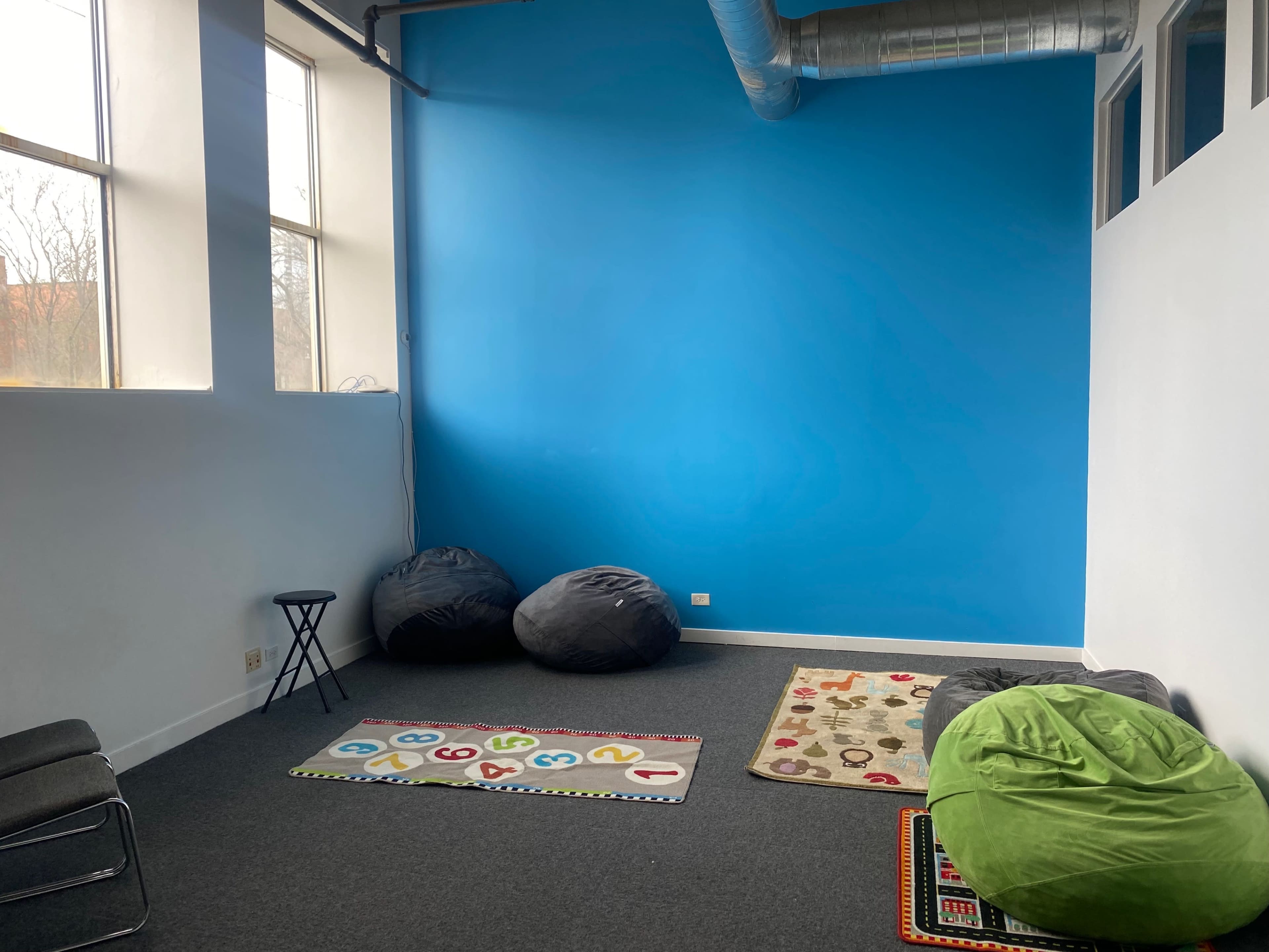 The room features a blue wall, two bean bag chairs, a numbered area rug, and a small table.