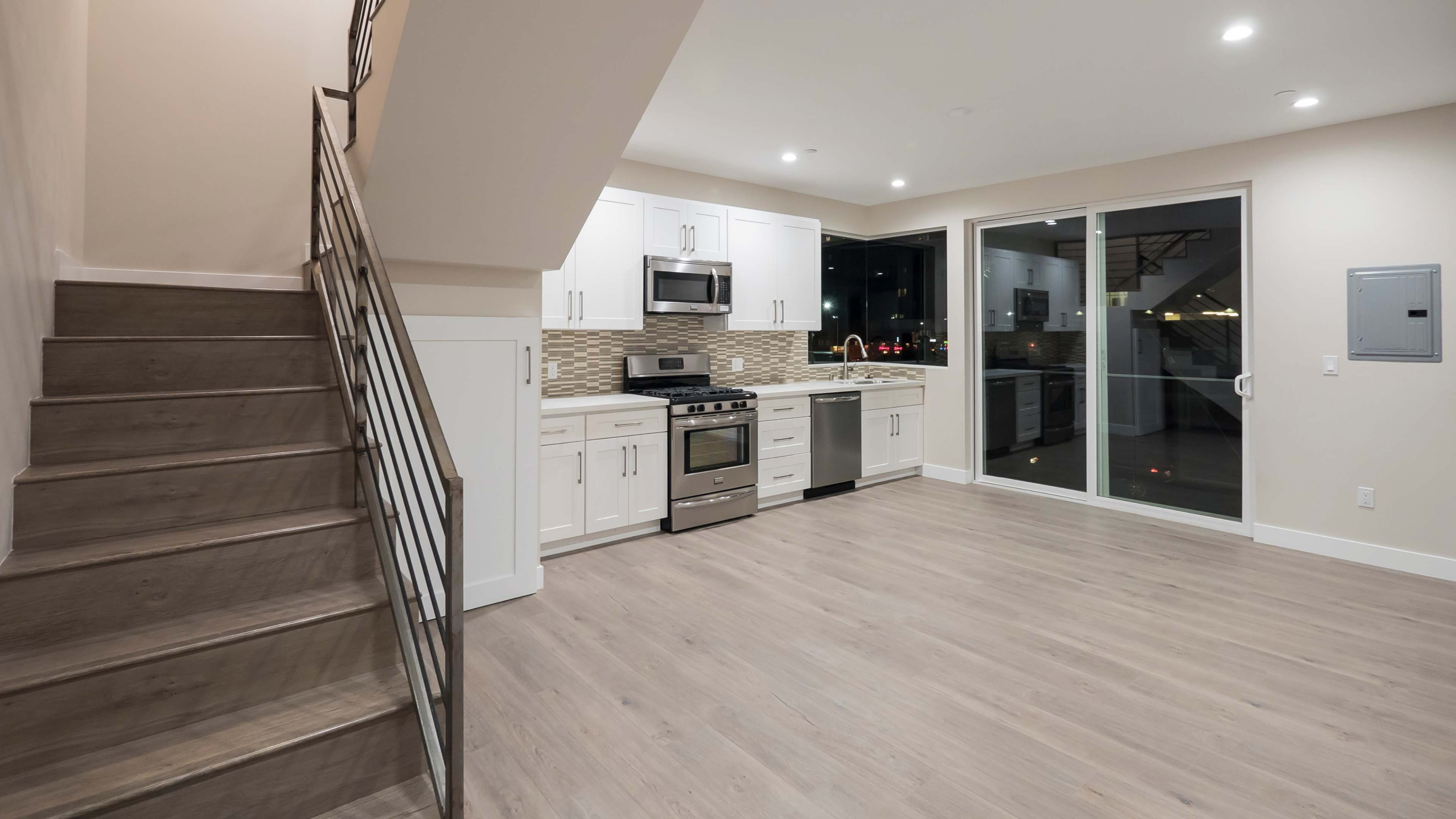 A modern kitchen and living area with white cabinetry, stainless steel appliances, and a staircase leading to an upper level.