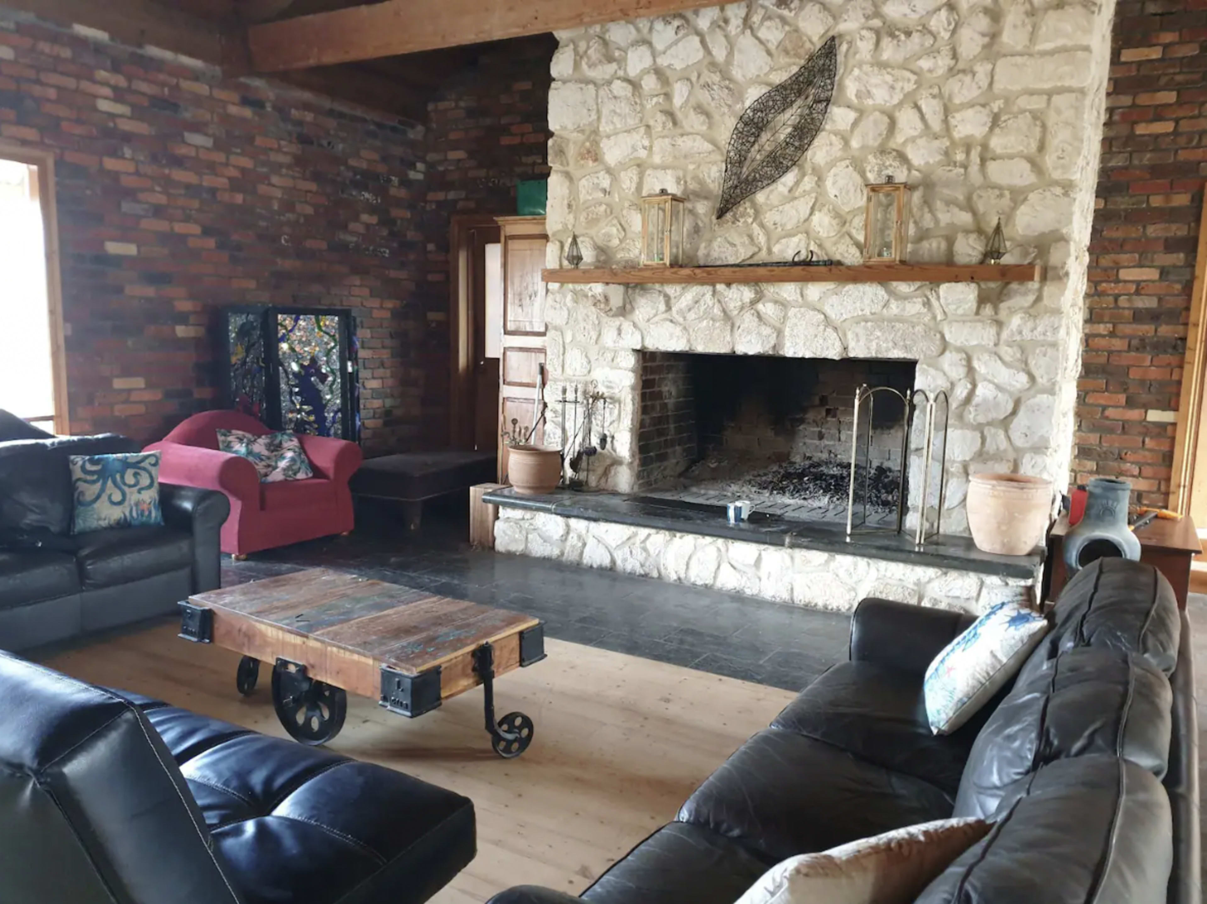 A living room featuring a stone fireplace, wooden beams, two sofas, a coffee table on wheels, and a decorative wall hanging.