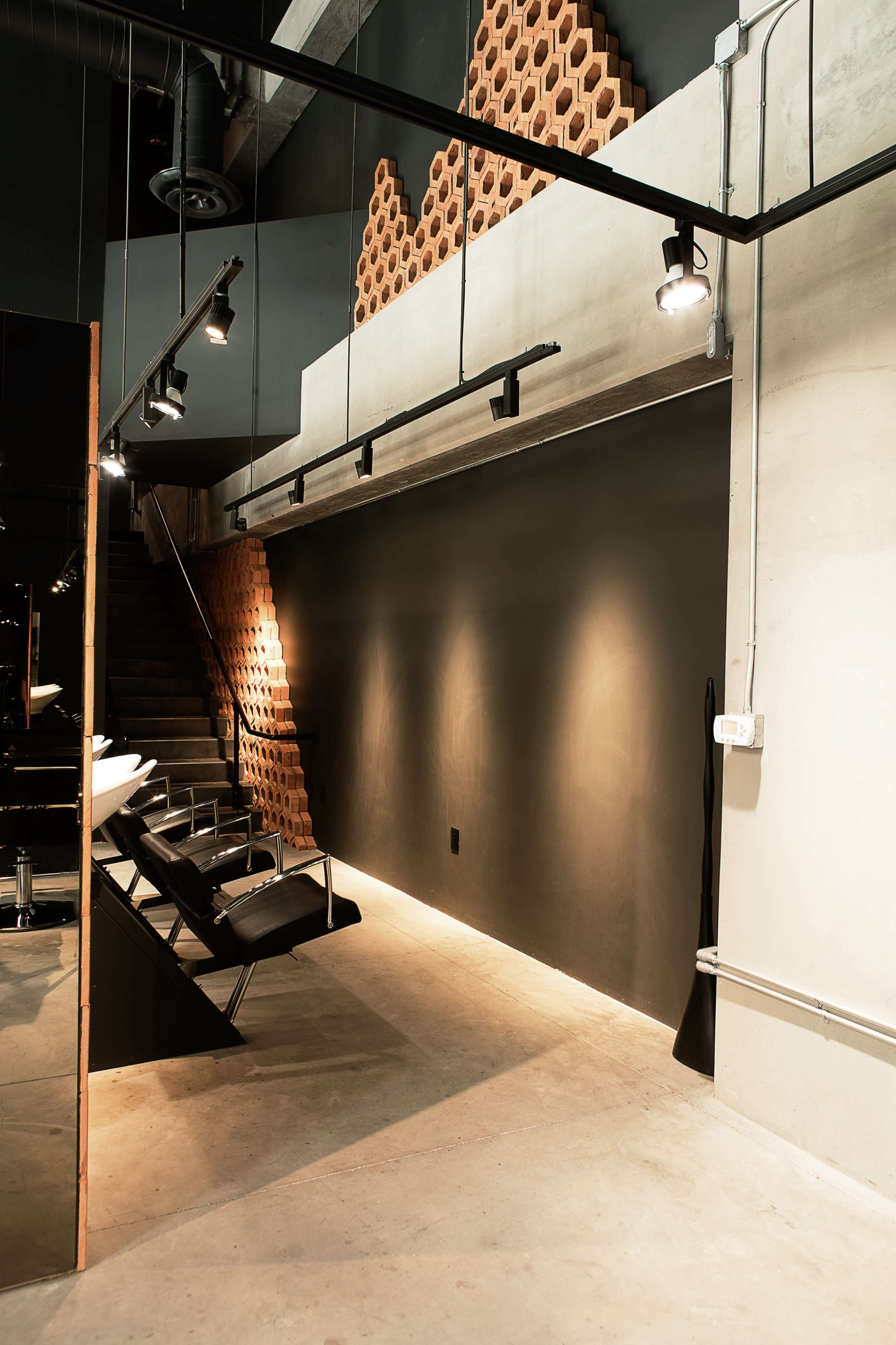 A modern interior with a dark wall, a row of sleek black chairs, and a staircase featuring a hexagonal pattern of wooden panels.