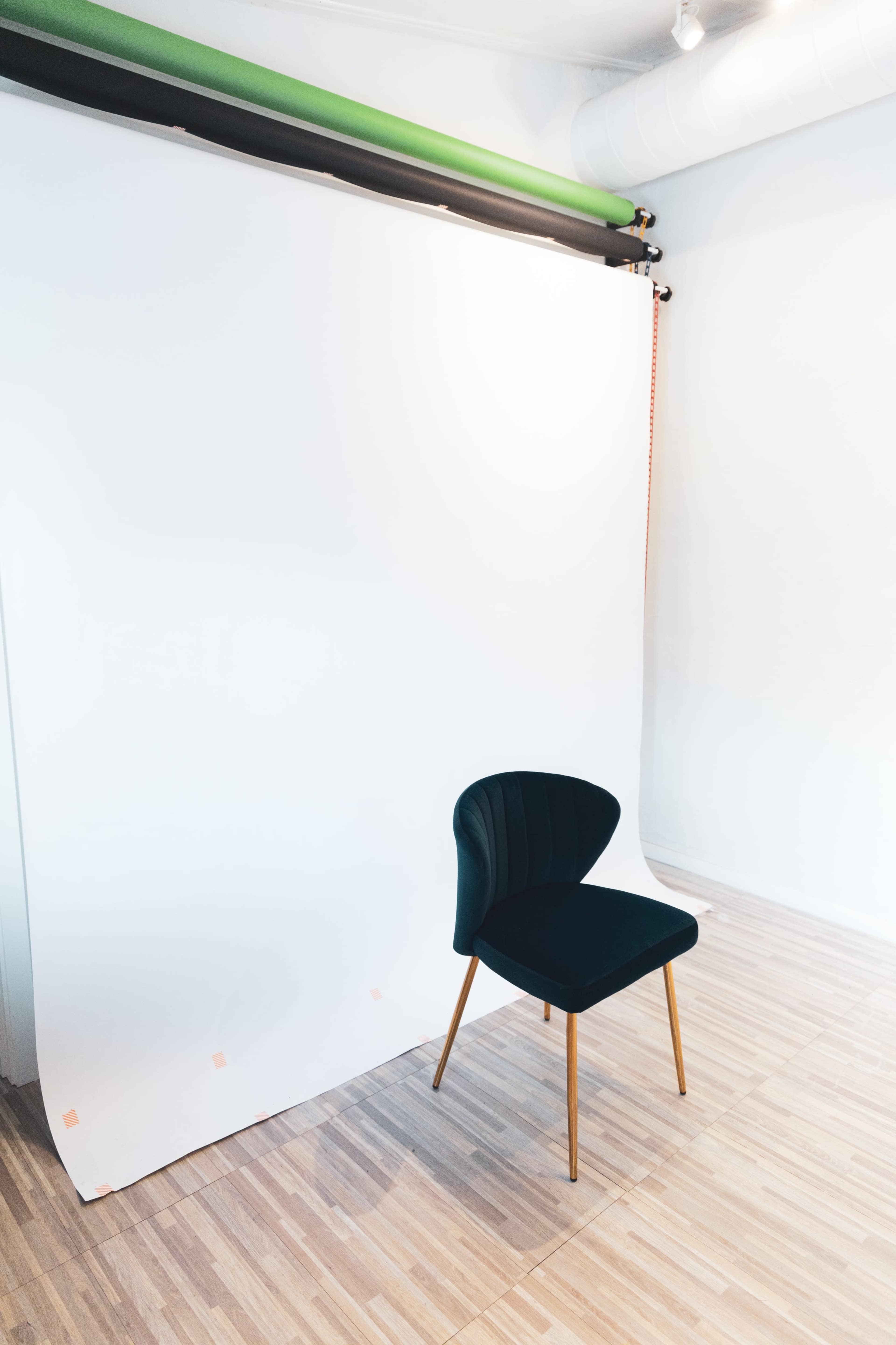 A single dark green chair is positioned in front of a plain white backdrop in a well-lit room.