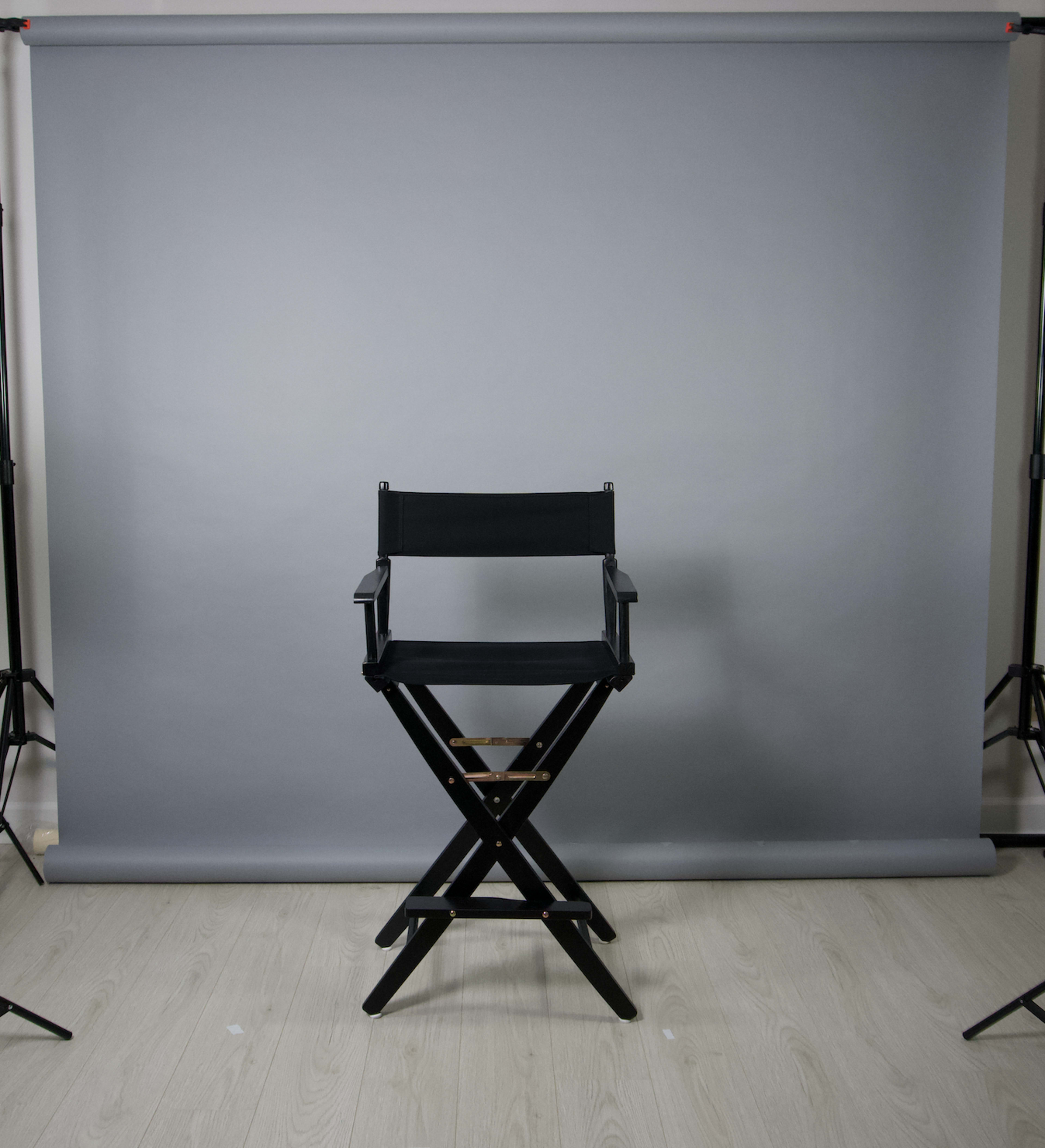 A black director's chair is positioned in front of a gray backdrop in a photography studio.