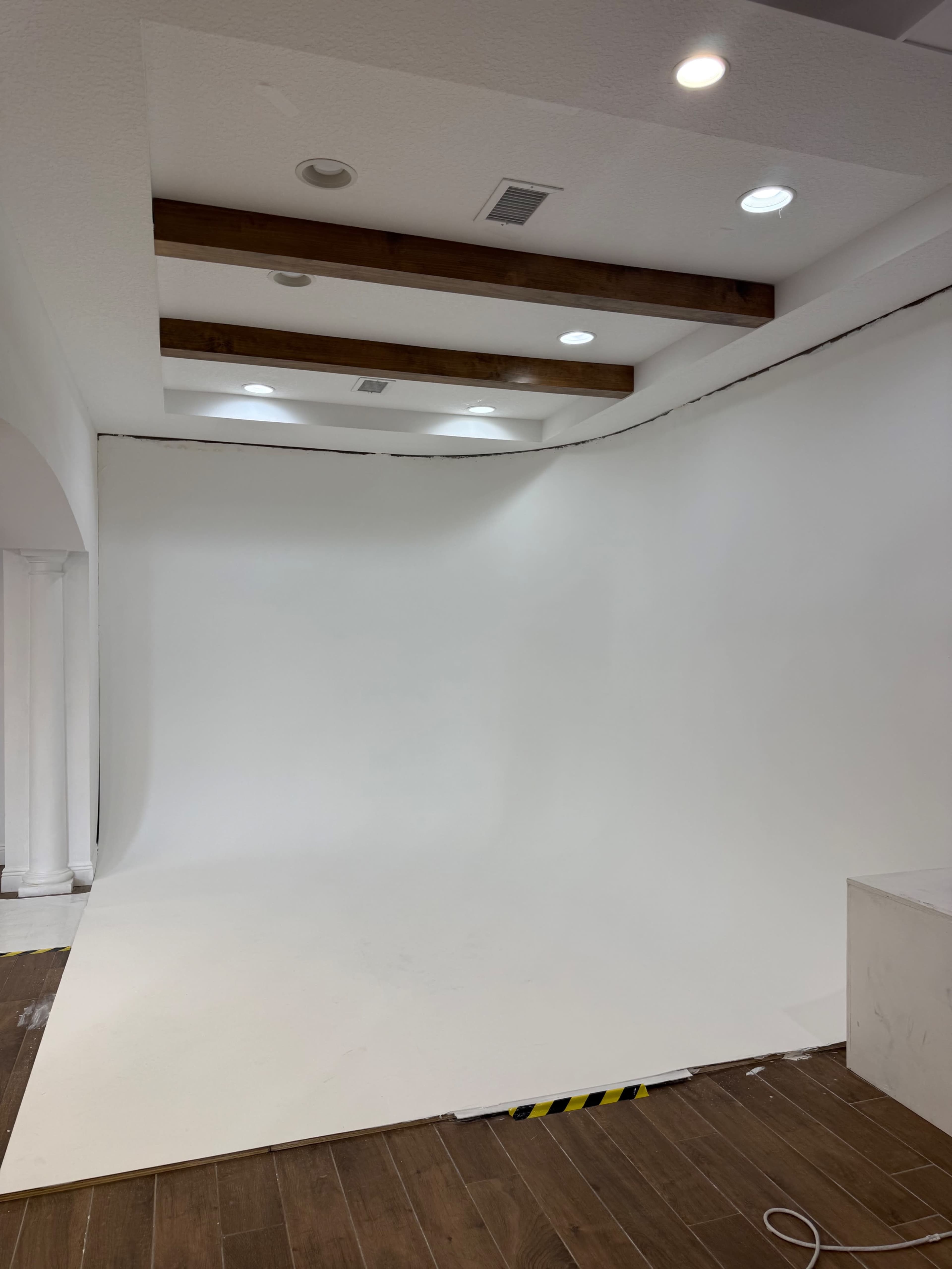 The image shows an empty photo studio with a white curved backdrop, wooden beams overhead, and columns in the background.