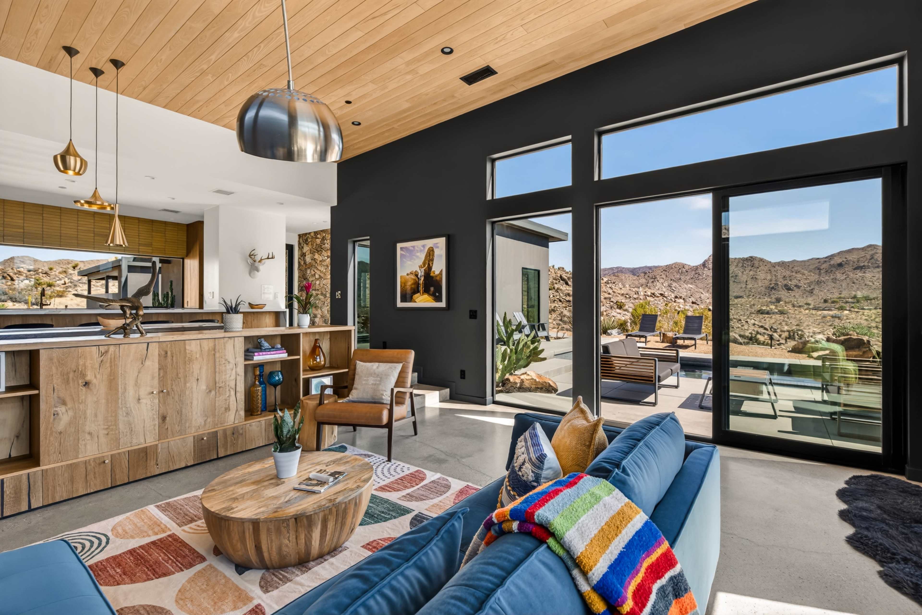 The image shows a modern living space with a view of rocky outdoor terrain, featuring a blue sofa, a round coffee table, and large windows allowing natural light to enter.
