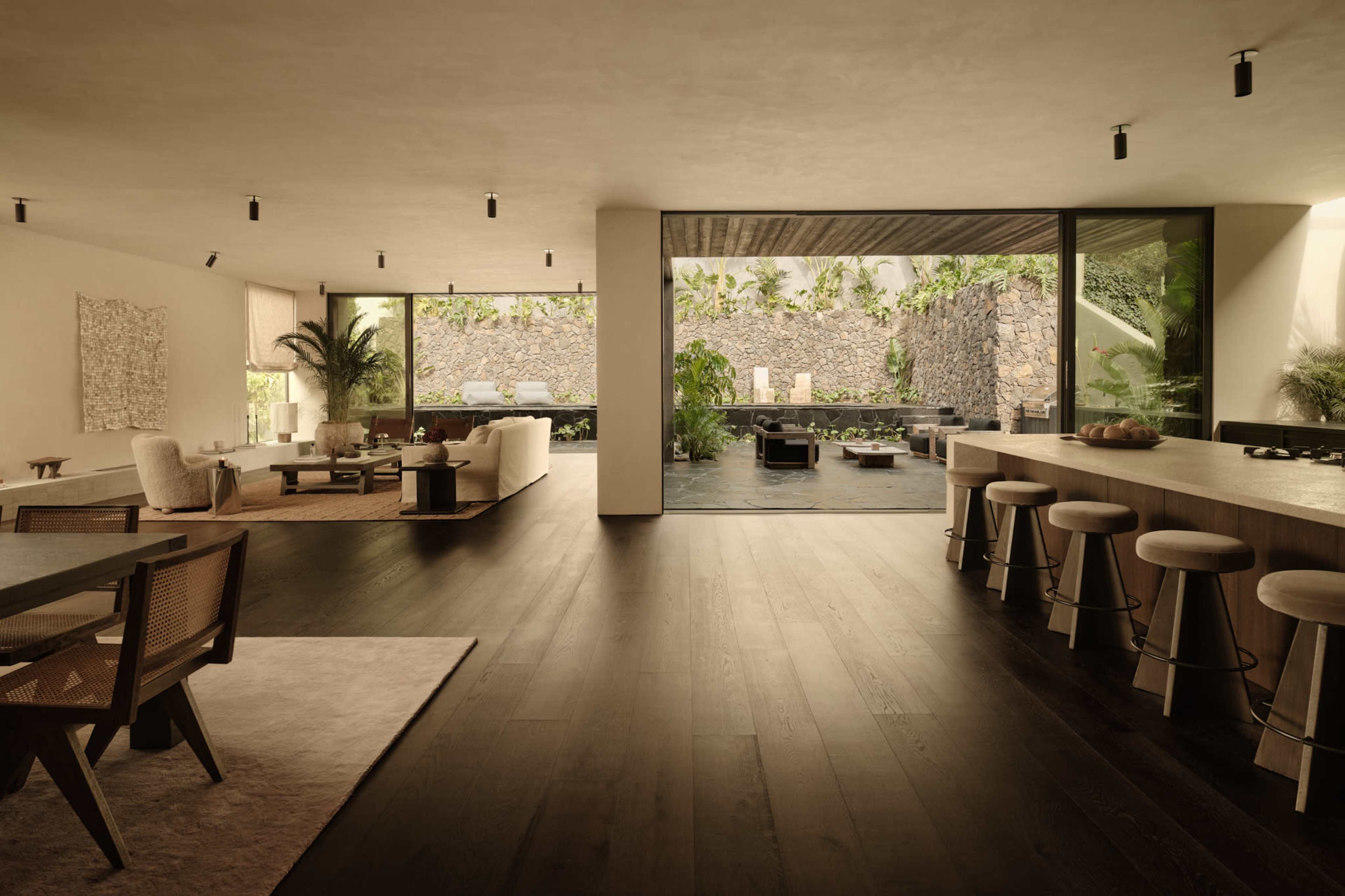 The image shows a modern indoor living space with large windows overlooking a lush outdoor area, featuring a serene water feature and minimalist furnishings.