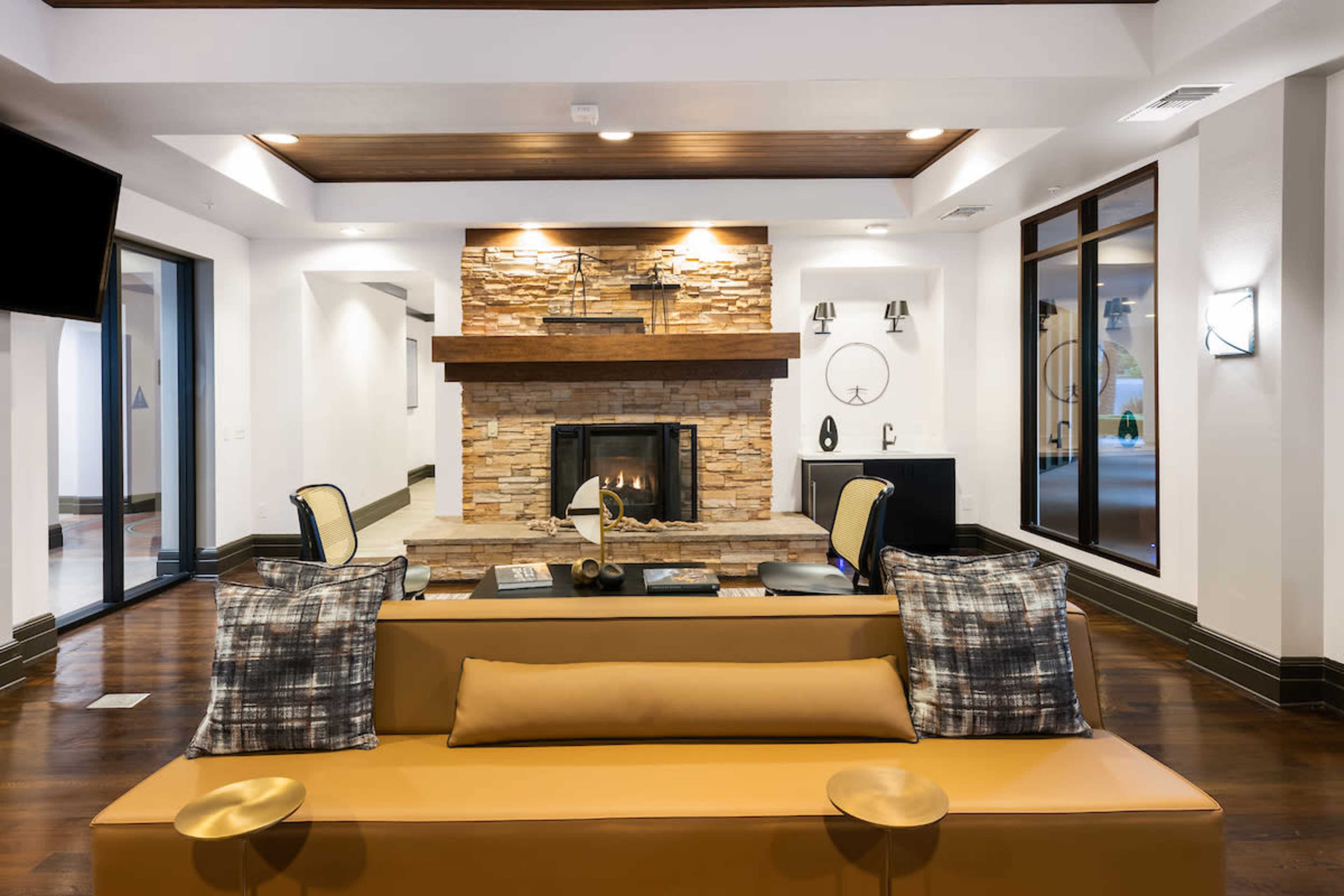 A modern living area with a stone fireplace, wooden ceiling, and a brown sofa decorated with patterned pillows.