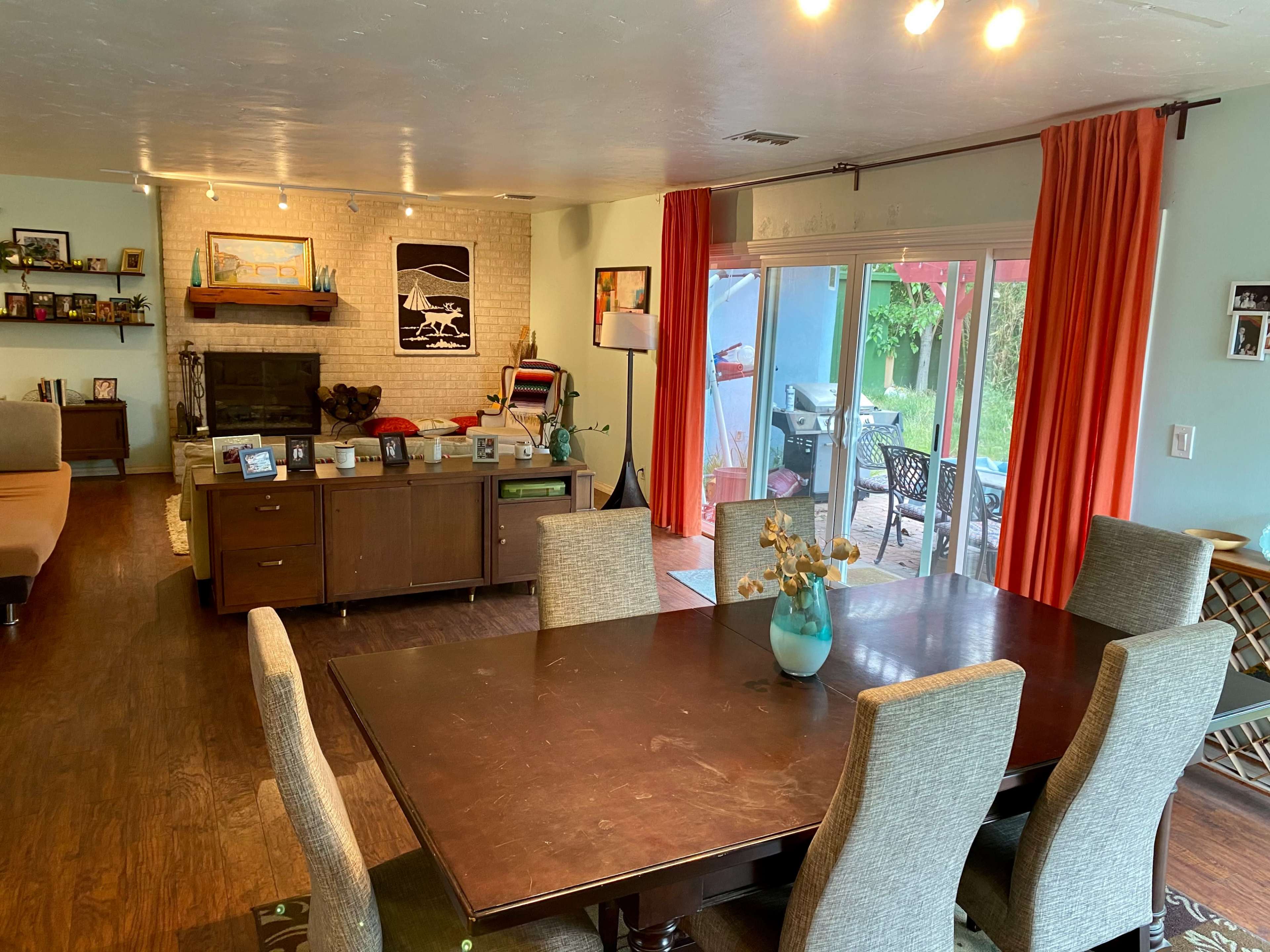 A spacious living and dining area features a wooden table with upholstered chairs, a modern kitchen island, and large windows leading to a patio.