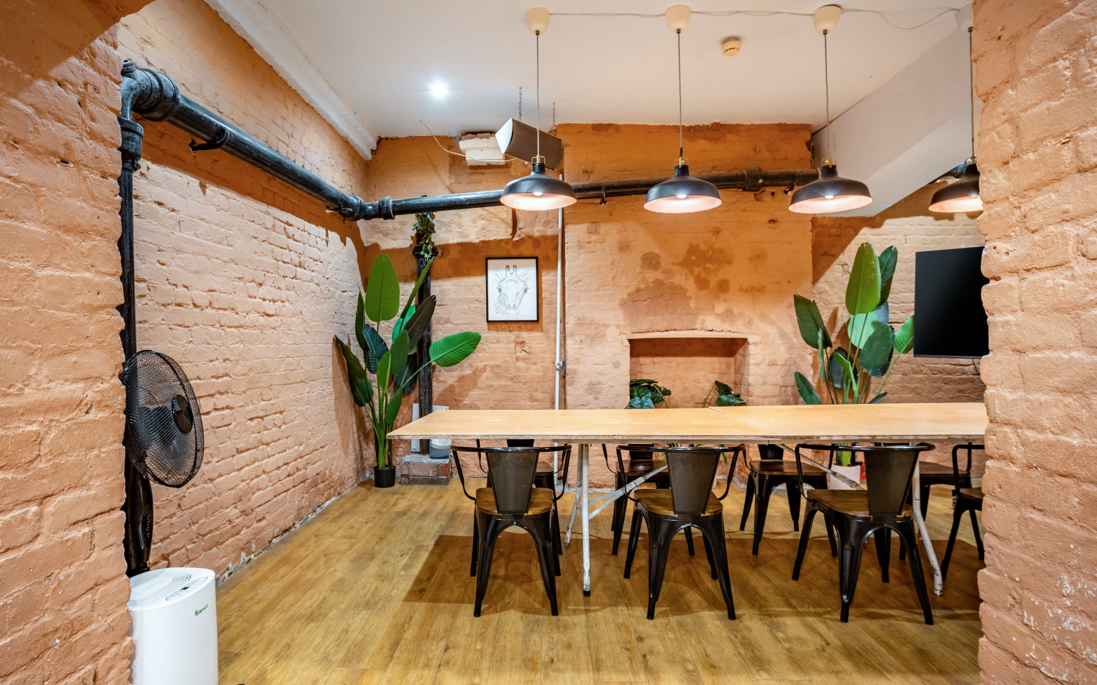 A spacious meeting room with a long wooden table, black chairs, and potted plants against textured orange walls.