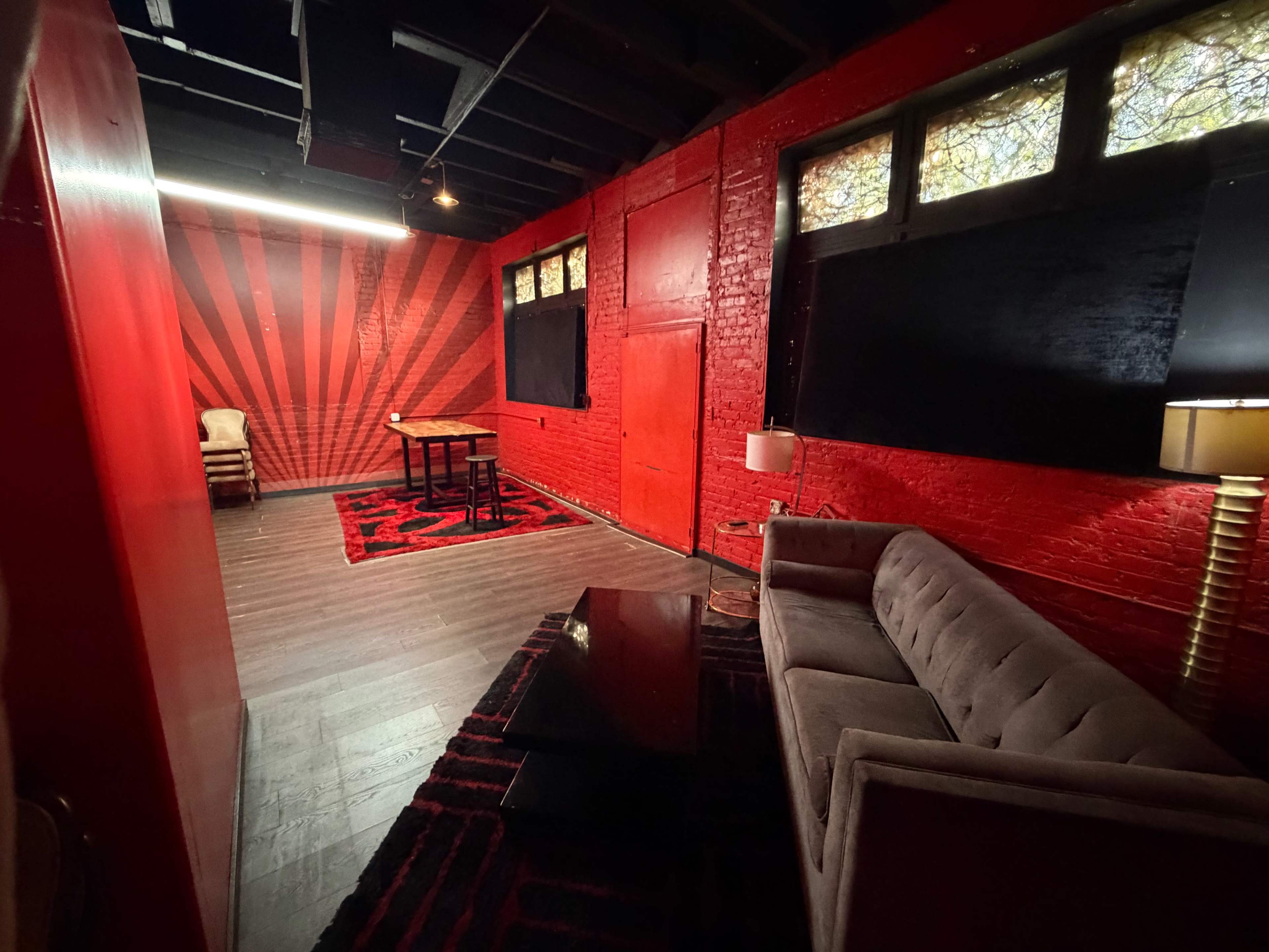 The room features red walls with a striped design, a dark rug, a plush sofa, and a table in the center under soft lighting.