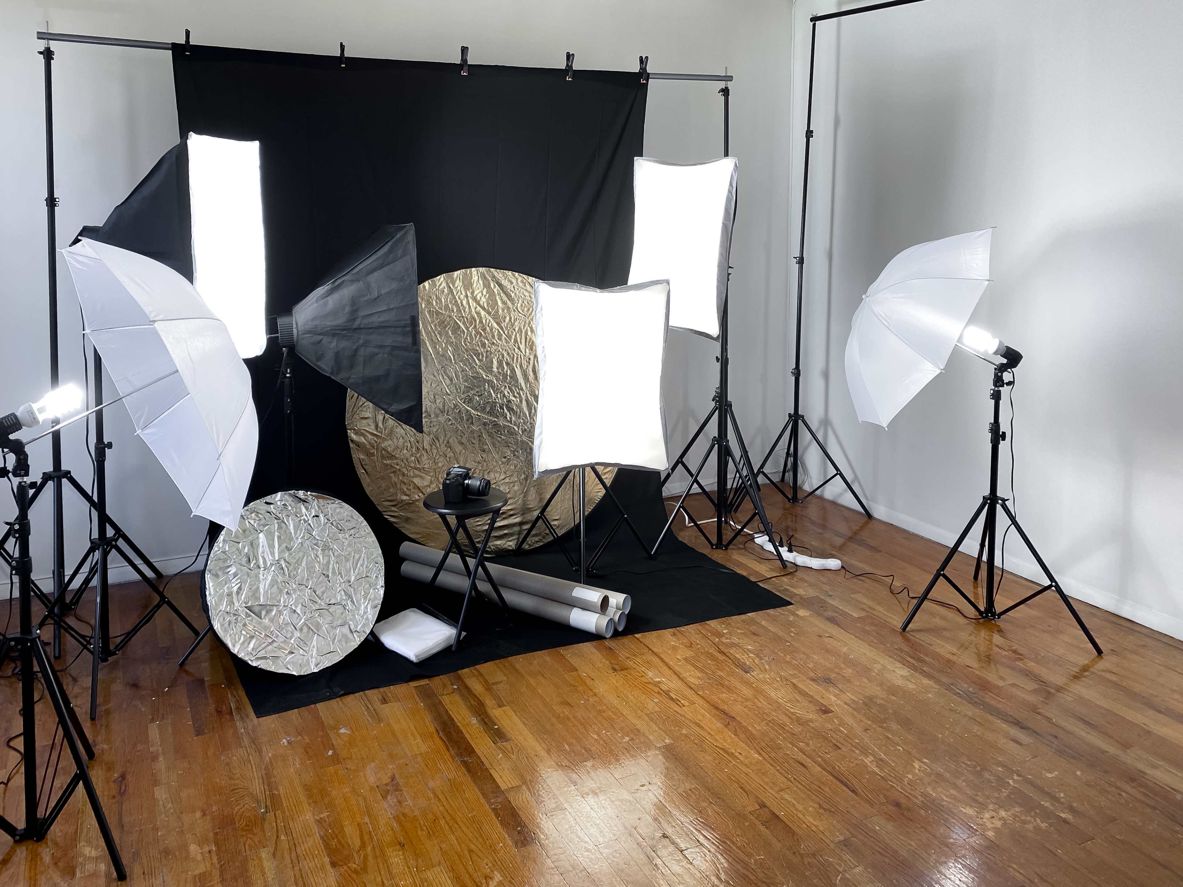 A photography studio setup with softbox lights, reflectors, and a black backdrop on a wooden floor.