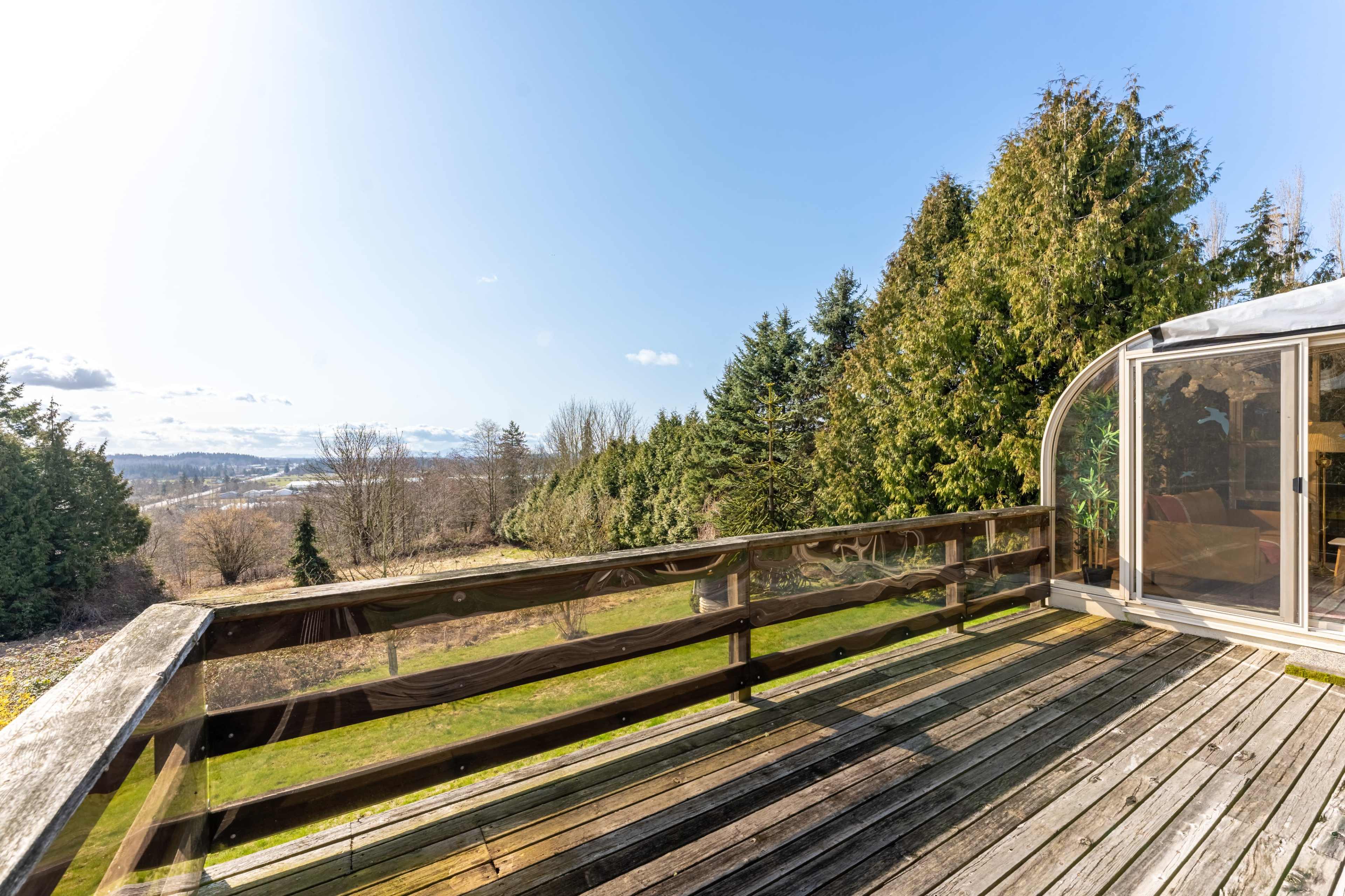 A wooden deck overlooking a grassy area and trees, with a view of distant hills under a clear sky.
