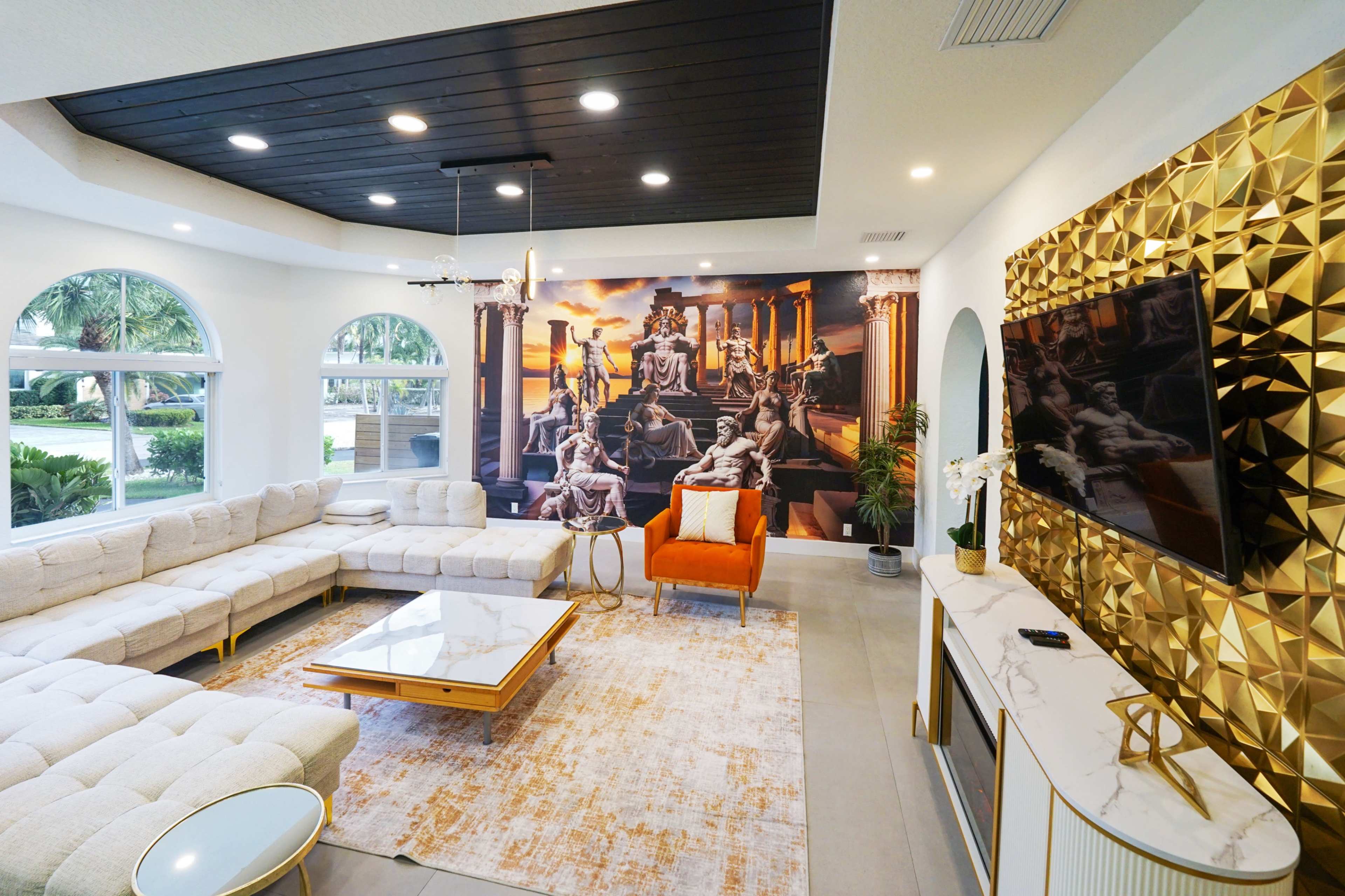 The image shows a modern living room featuring a large sectional sofa, a coffee table, a decorative wall mural, and a golden accent wall with a television.