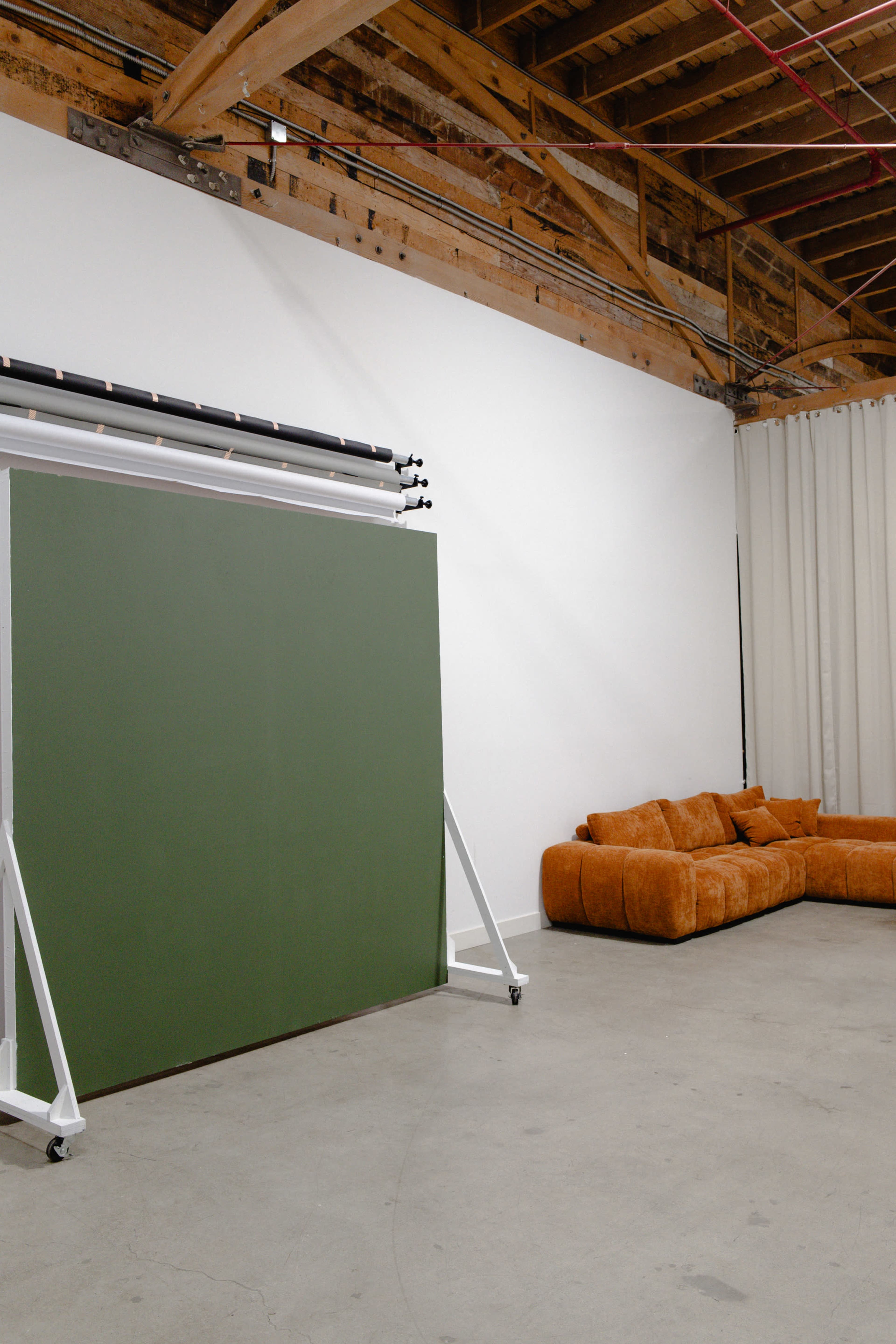 The image shows a spacious room featuring a green backdrop on wheels and an orange sofa along the wall.