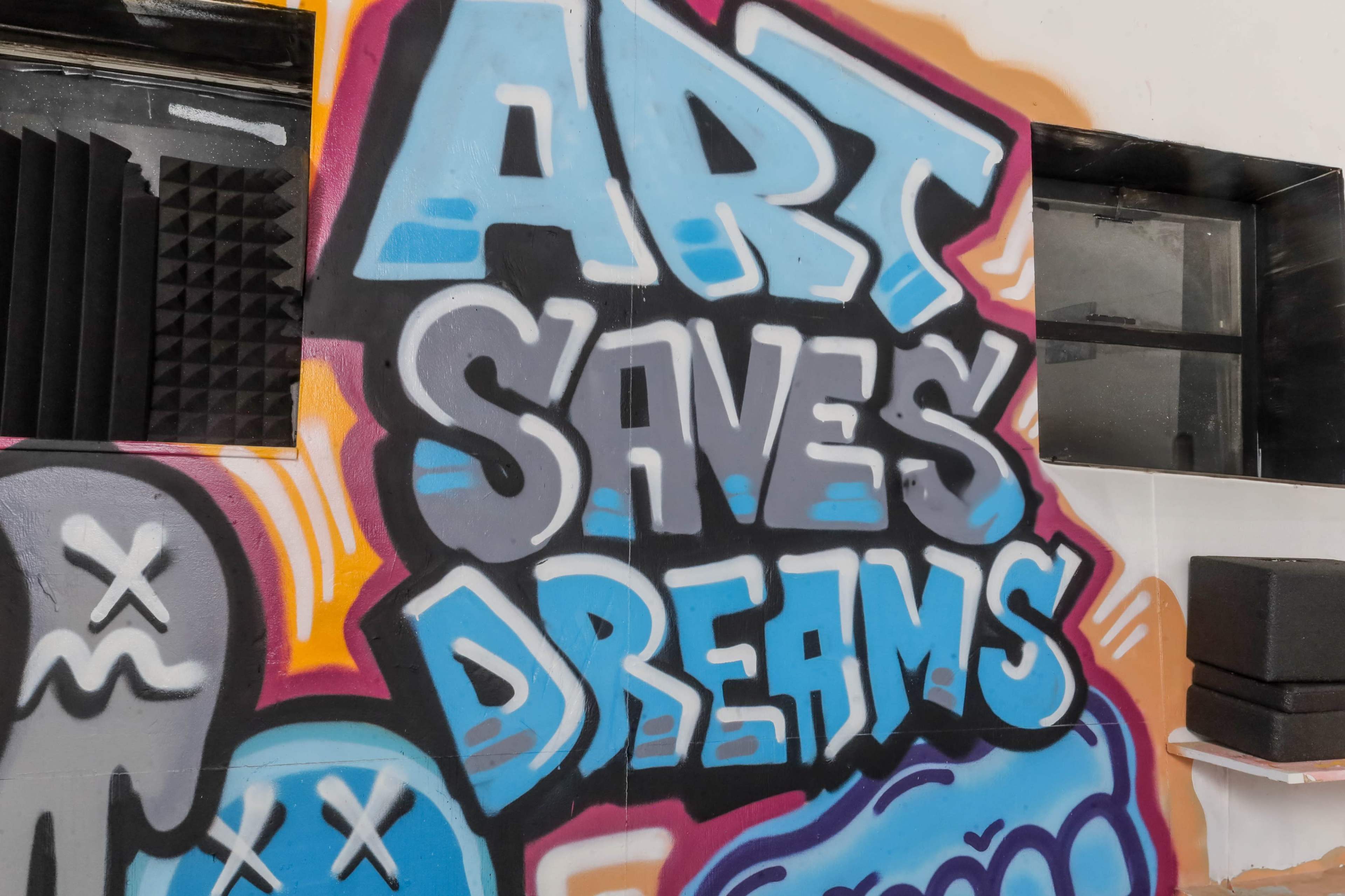 The image features a mural on a wall that reads "ART SAVES DREAMS" in bold, colorful graffiti letters.